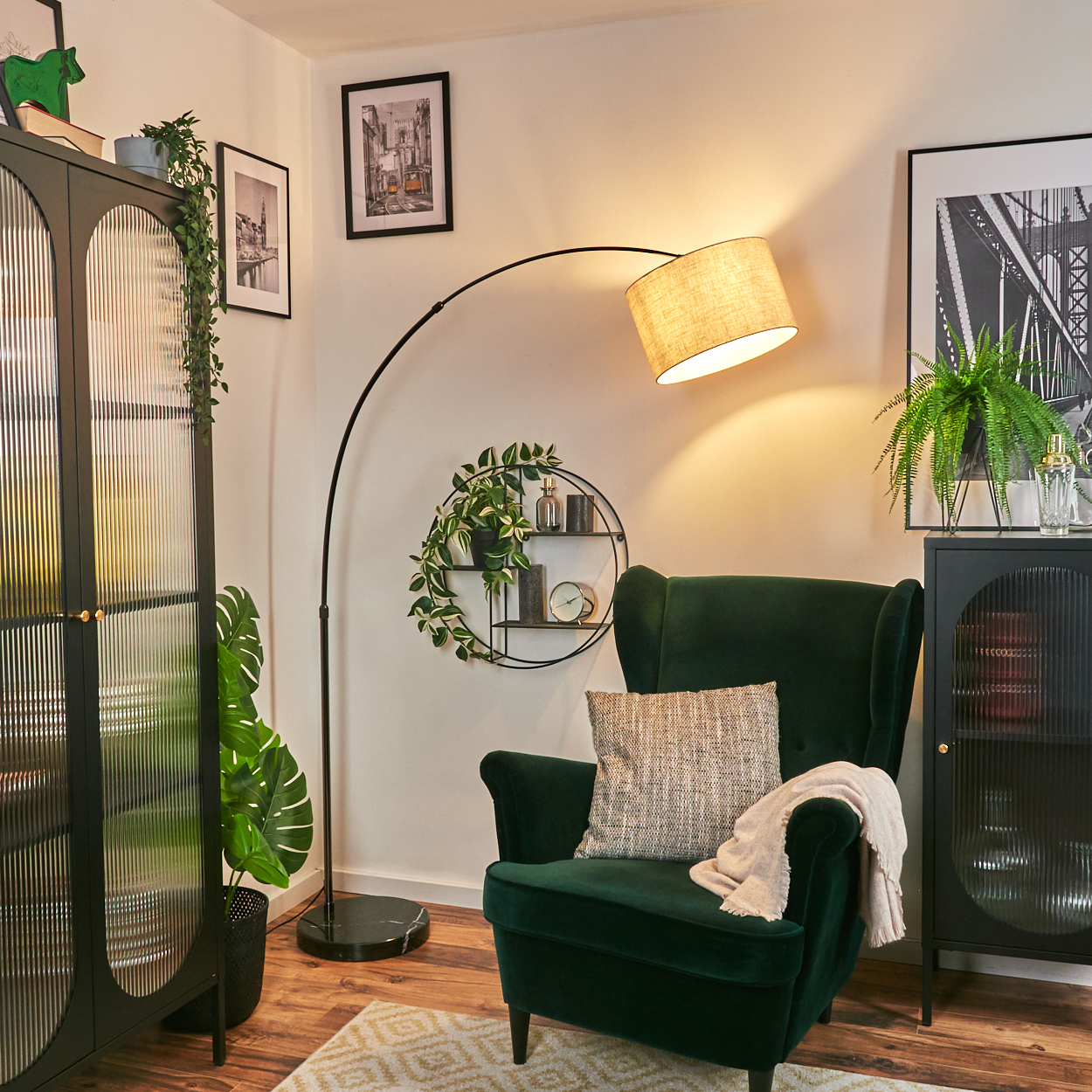 Ein grüner Sessel mit Kissen und Decke steht unter einer Lampe. Schrank und Bilder sind an den Seiten. Eine Pflanze befindet sich neben dem Stuhl.