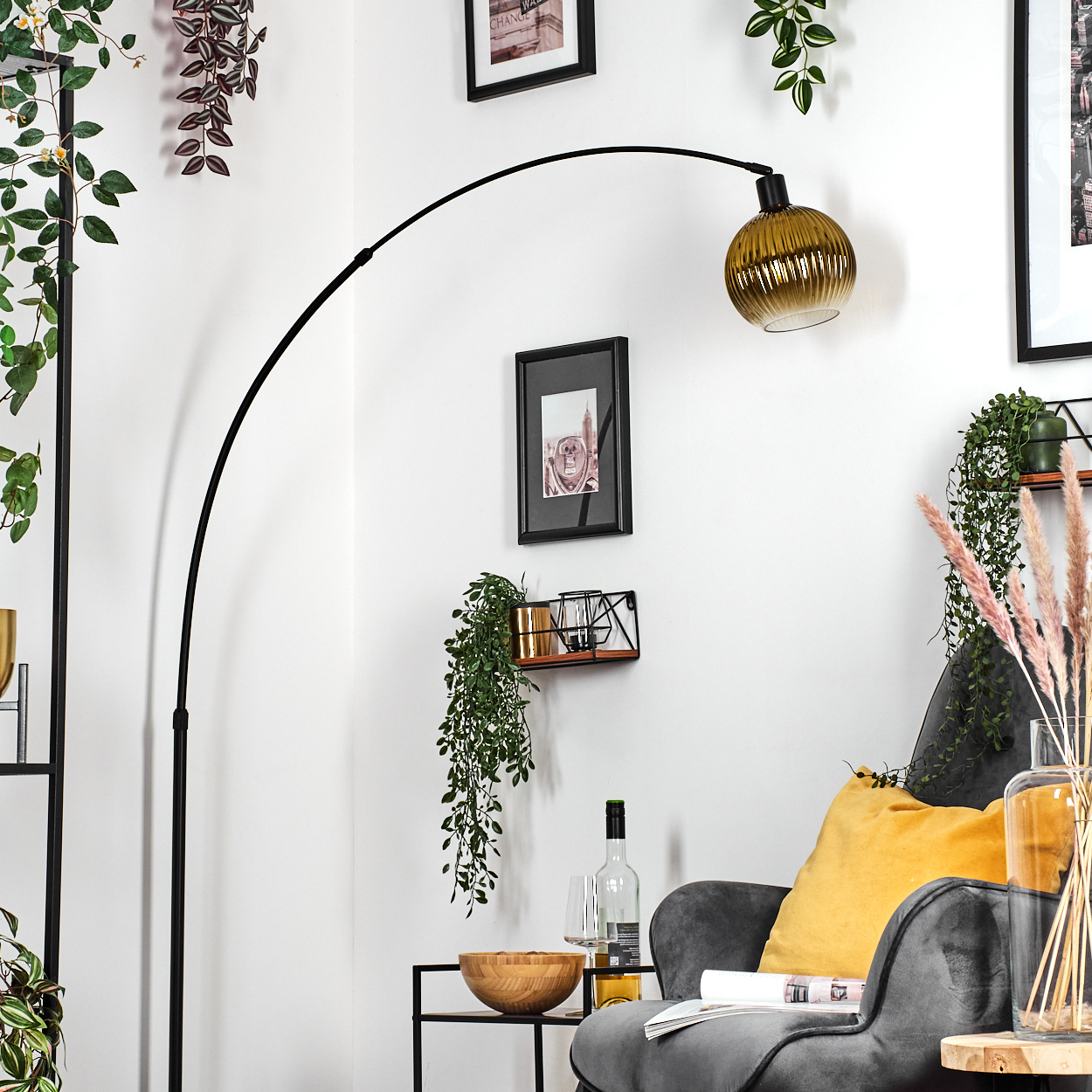 Ein modernes Wohnzimmer mit schwarzer Bogenlampe, grauem Sessel, gelbem Kissen und Zierpflanzen. Ein Tisch hält eine Schüssel und Wein.