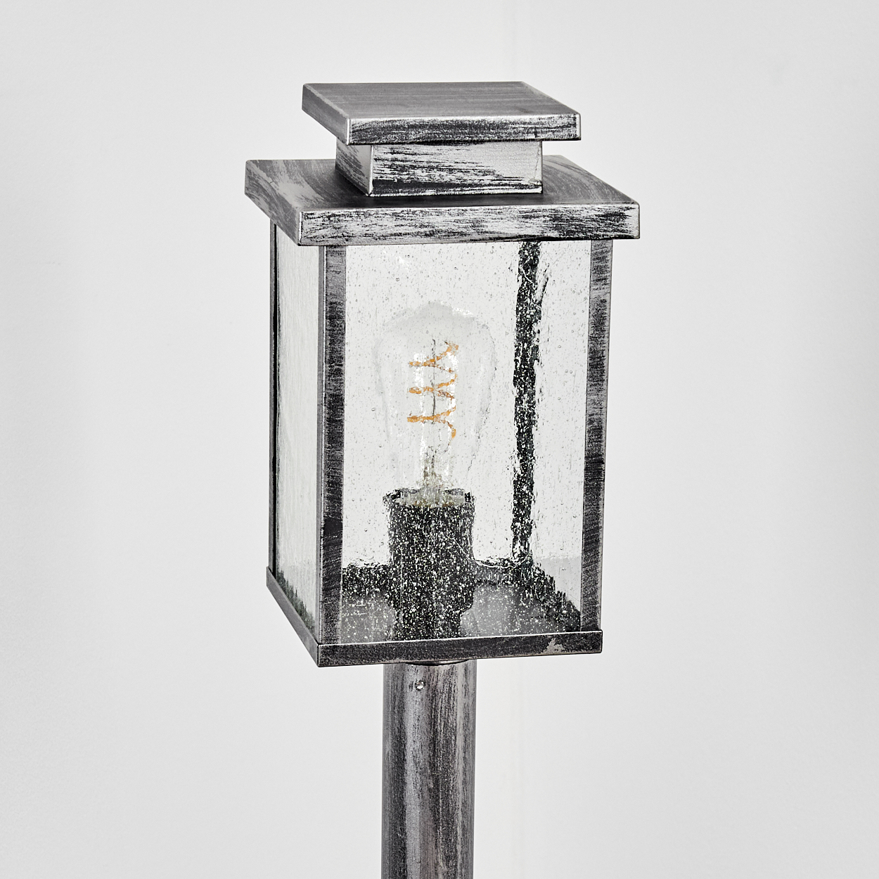 Eine dekorative Außenlampe. Sie hat einen quadratischen Glaskörper mit einer Glühbirne im Inneren, die auf einer Metallstange montiert ist.
