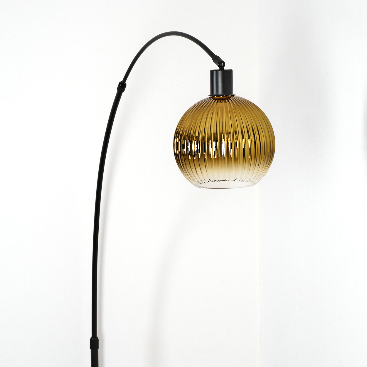 Eine moderne Stehlampe mit einem schwarzen, gebogenen Arm und einem gerippten, bernsteinfarbenen Glasschirm. Der Hintergrund ist eine weiße Wand.
