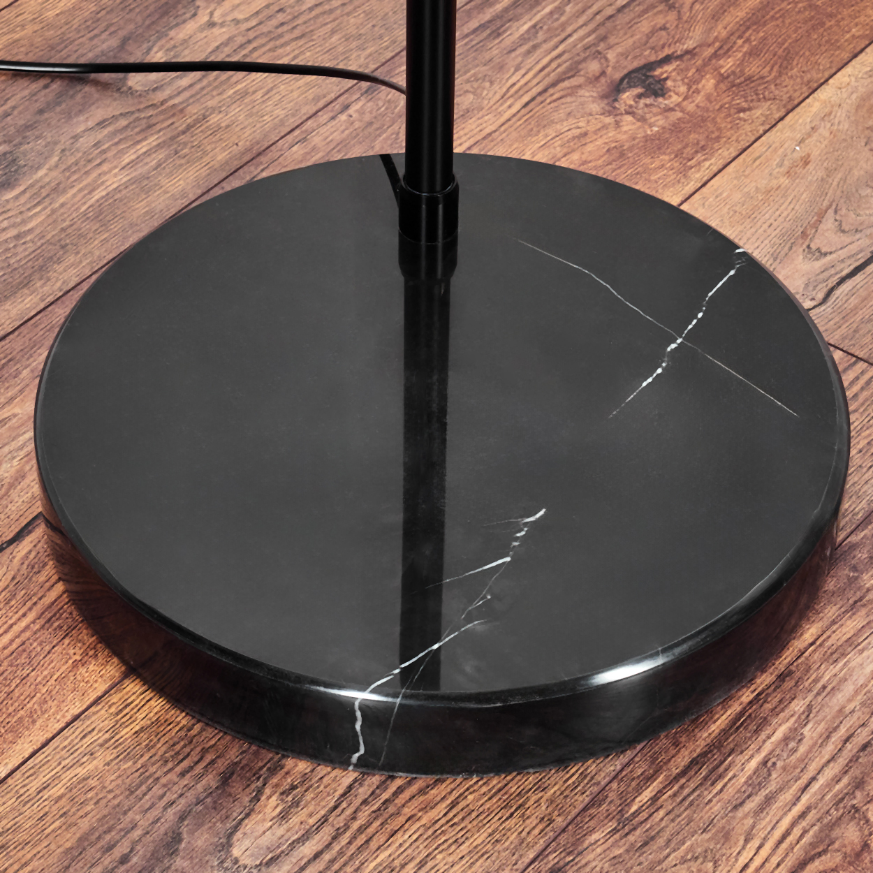 Nahaufnahme eines schwarzen Marmor-Lampenfußes auf einem Holzboden. Die Basis hat weiße Adern und eine schwarze Stange.