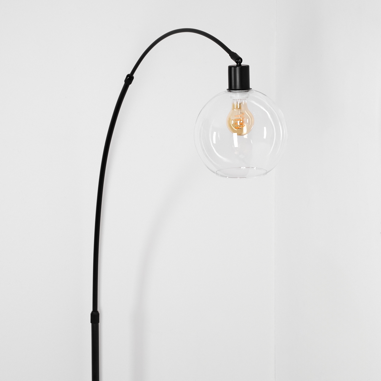 Eine moderne schwarze Lampe mit einem klaren Glaskolben, der eine Glühbirne umschließt, vor einer weißen Wand.