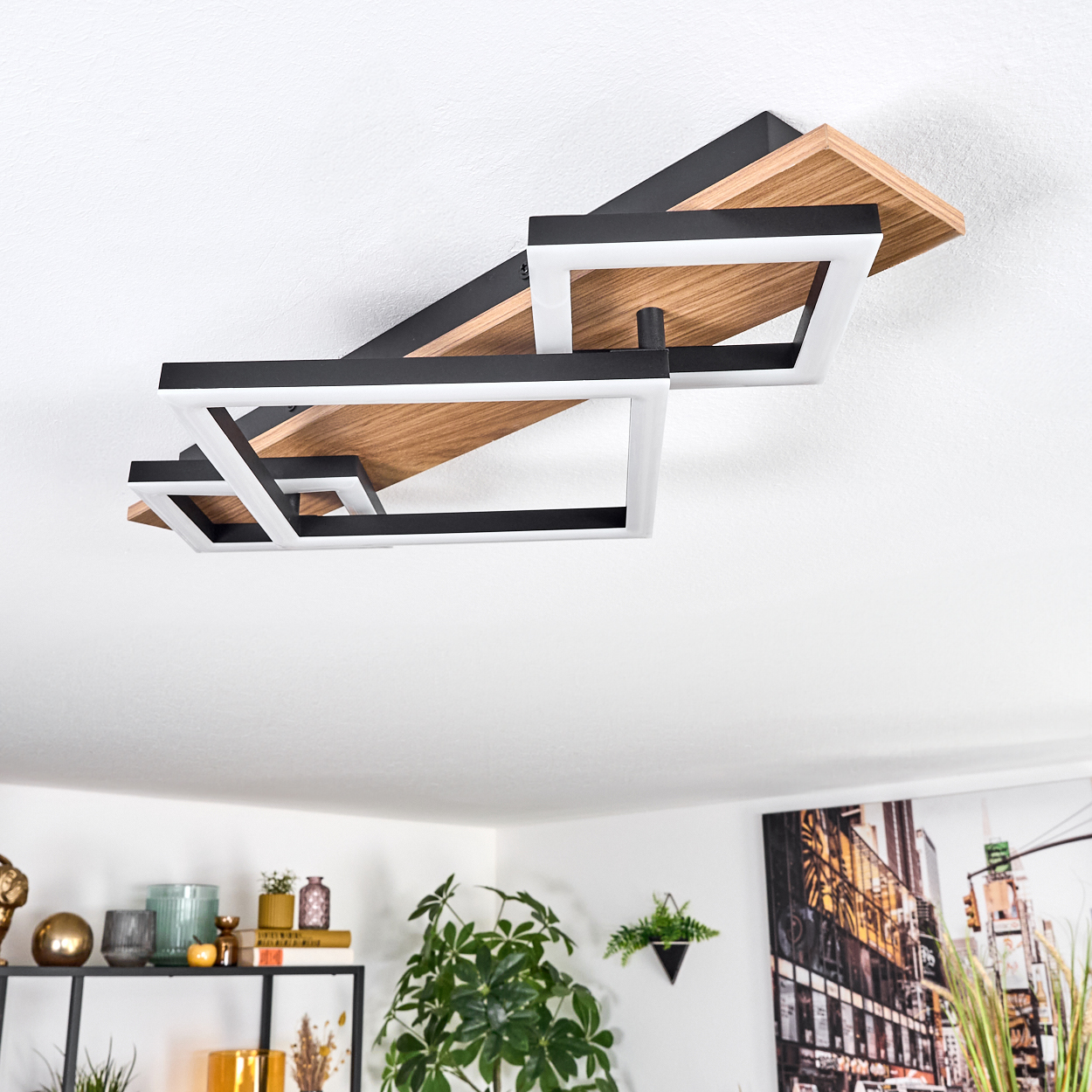 Moderne Deckenleuchte mit Holz- und schwarzen Elementen. Darunter ein Regal mit Dekoration und Pflanzen sowie ein Stadtbildgemälde.