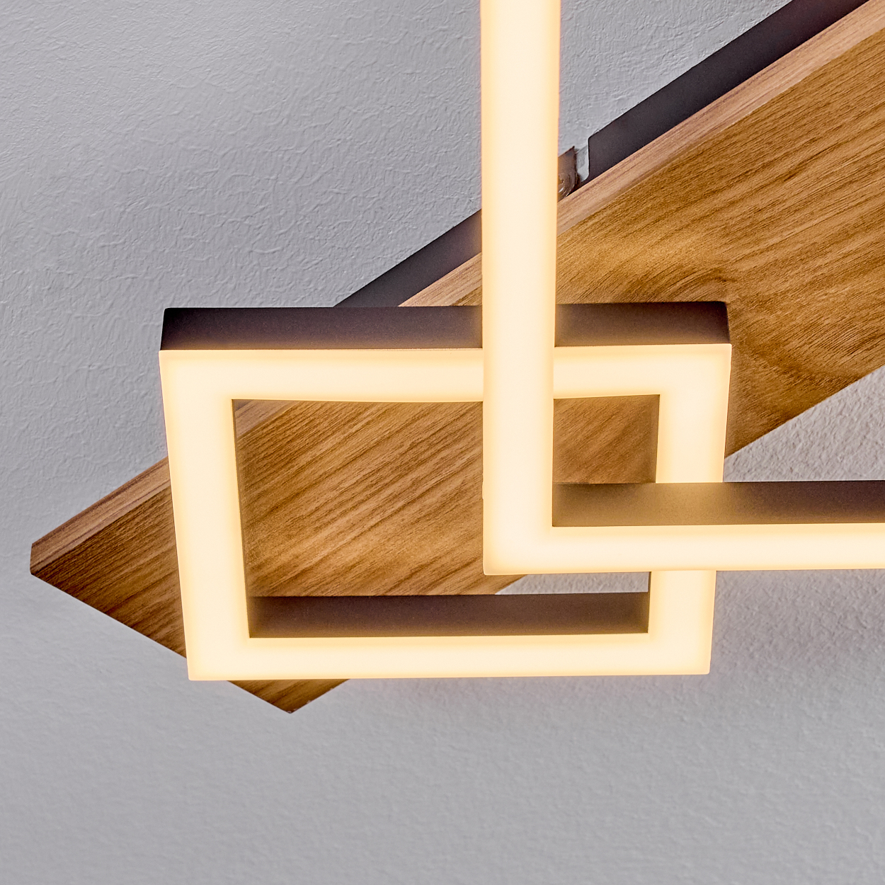 Geometrische moderne Deckenleuchte. Holzpaneele und sich kreuzende, beleuchtete weiße Rechtecke und Linien vor hellgrauer Wand.