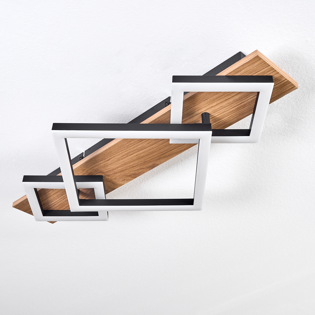Eine moderne Deckenleuchte mit drei weiß umrahmten Quadraten und Holzbrettern vor einer weißen Decke.