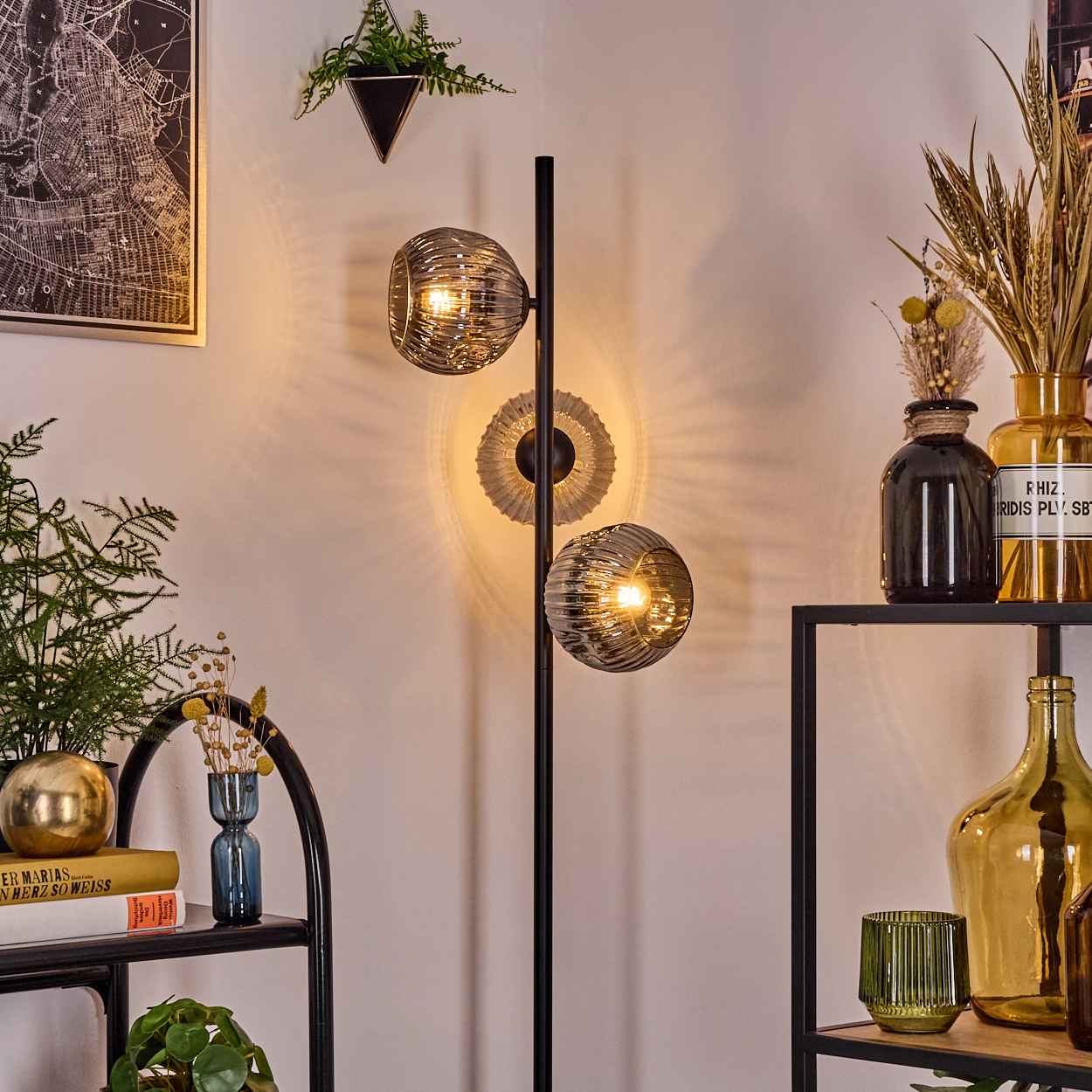 Ein modernes Wohnzimmer mit schwarzer Lampe, Regalen mit Vasen, Pflanzen und einer Karte an der Wand. Die Lampe hat zwei leuchtende Kugeln.