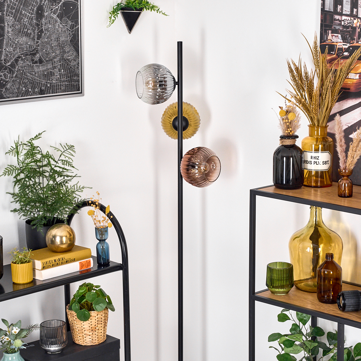 Raumecke mit Regalen, Pflanzen und Stehlampe. Es gibt Glaskugeln, Vasen und Dekorationsartikel. Eine Karte hängt an der Wand.