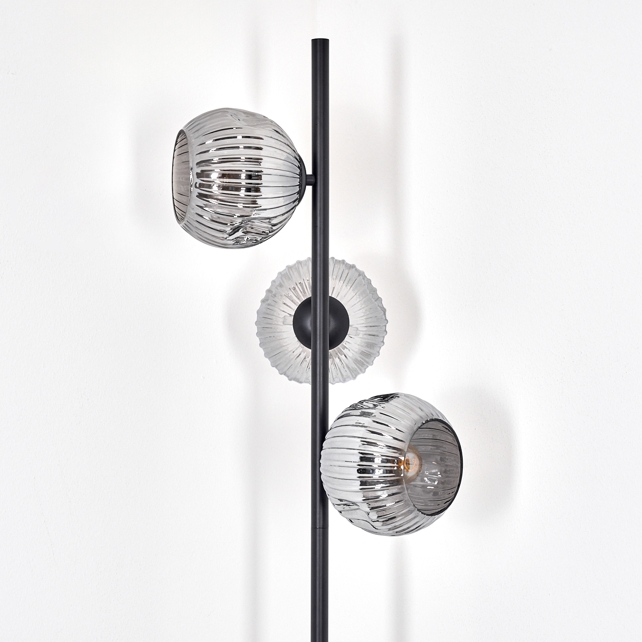 Eine moderne Lampe mit drei Glasschirmen in einem weißen Raum. Die Schirme sind rund, und die Lampe ist schwarz. Der Hintergrund ist weiß.