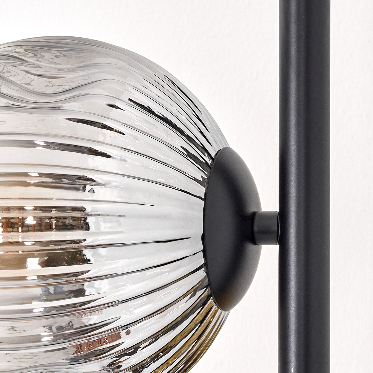 Nahaufnahme einer Lampe mit klarem, geripptem Glaskugel und schwarzem Metallrahmen vor weißem Hintergrund.