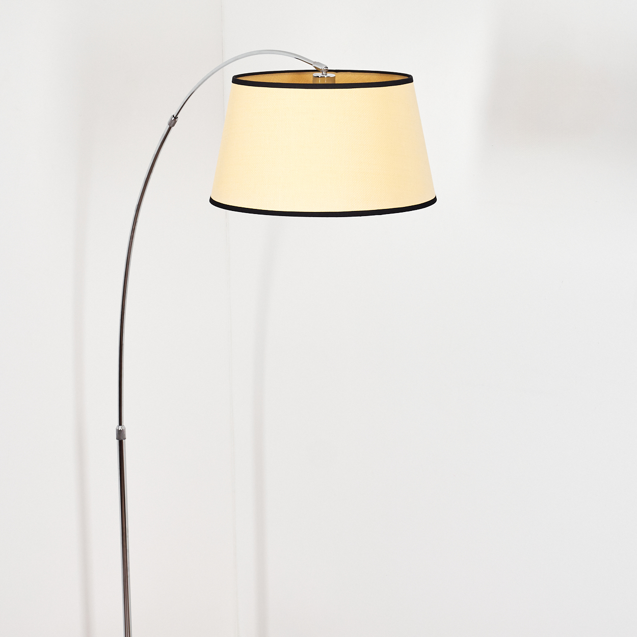 Eine moderne Stehlampe mit beigem Lampenschirm und schwarzem Rand vor einer weißen Wand.
