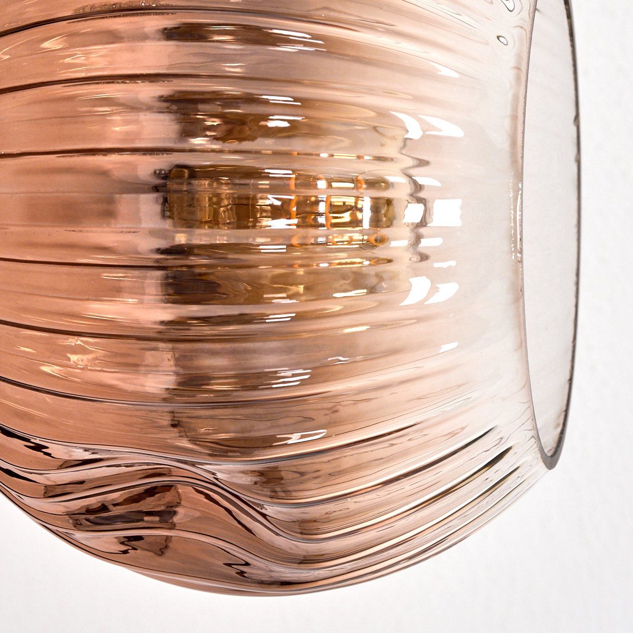 Nahaufnahme eines Glasobjekts mit horizontalen Rillen. Es hat einen Bronzeton. Licht reflektiert von der Oberfläche.