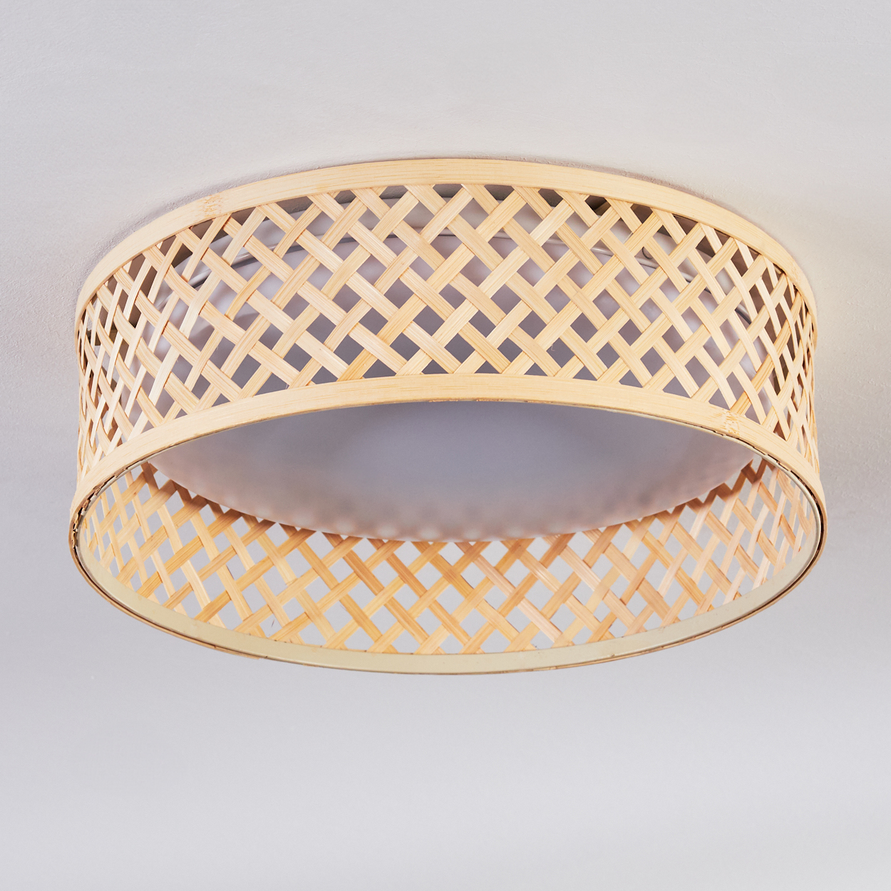 Eine gewebte Deckenlampe aus Bambus hängt an einer weißen Decke. Die Lampe hat eine zylindrische Form mit einem gemusterten Schirm.