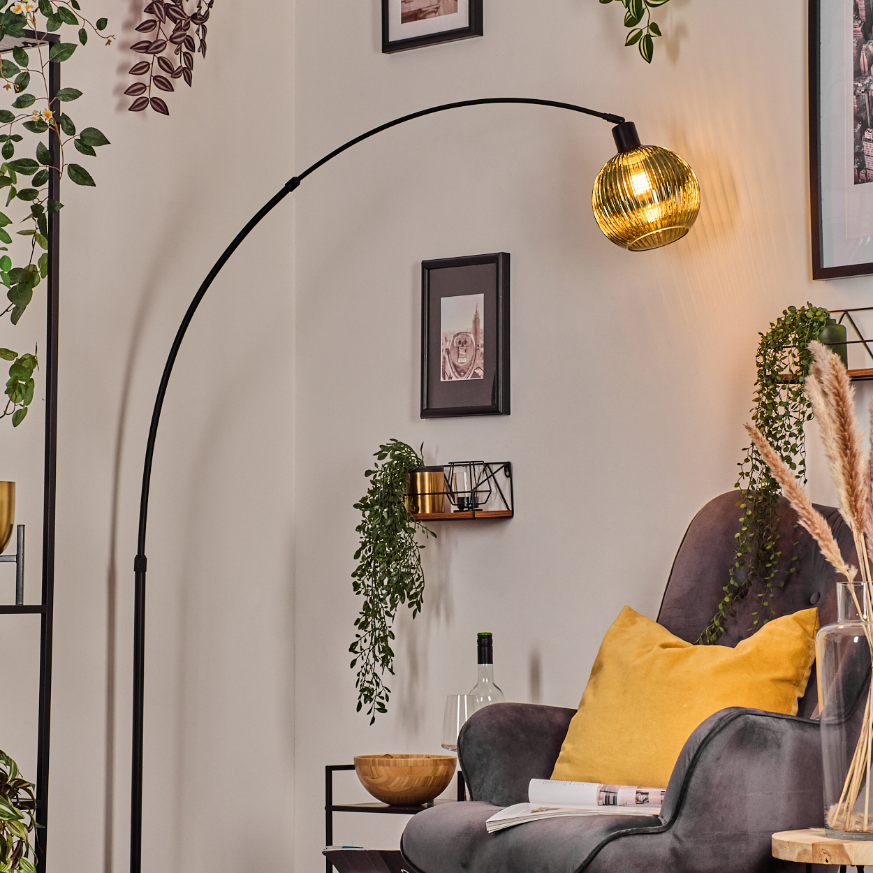 Ein modernes Wohnzimmer mit schwarzer Bogenlampe, grauem Sessel, gelbem Kissen und Zierpflanzen. Eine Holzschale und eine Zeitschrift sind sichtbar.