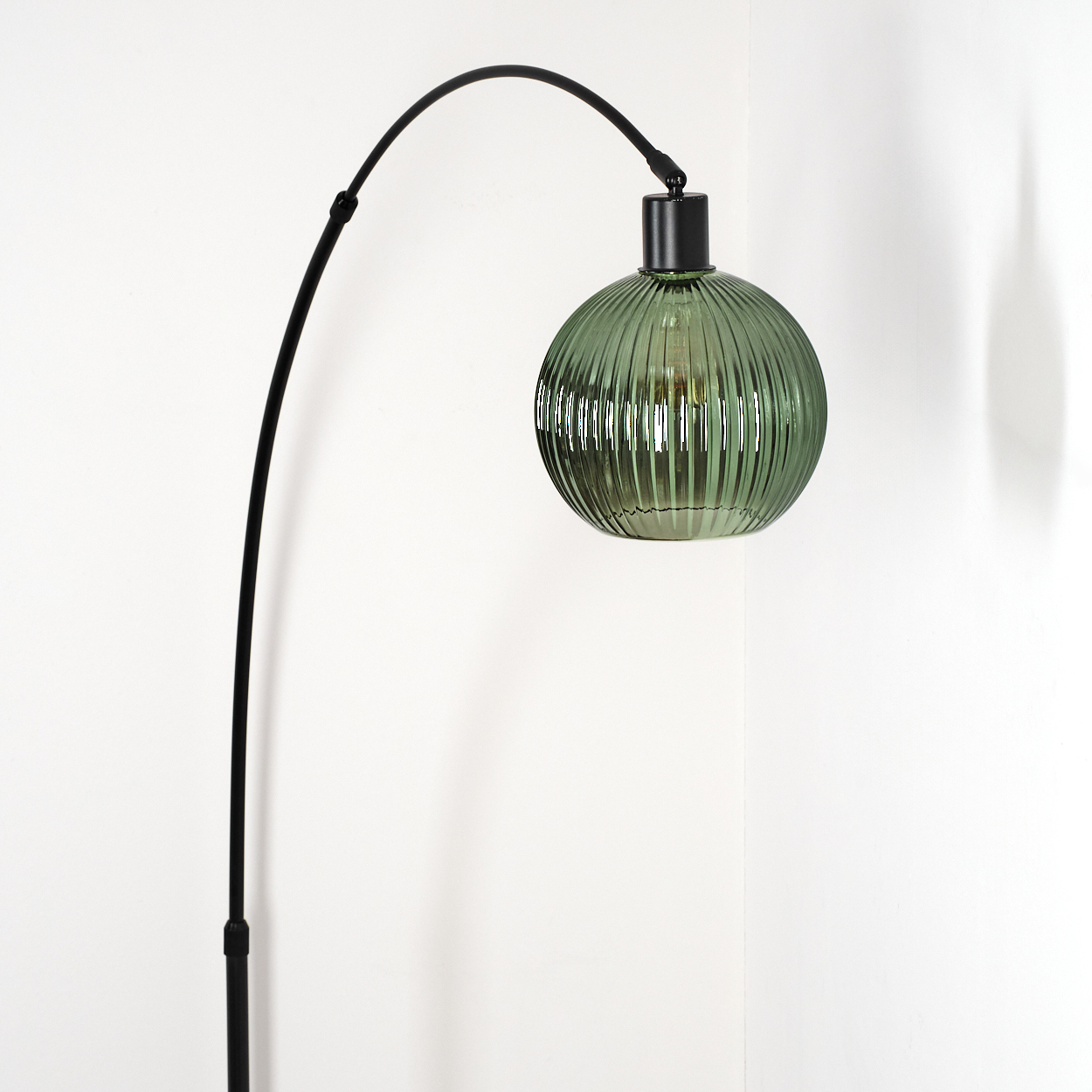 Eine moderne Bogenlampe mit grünem Glasschirm. Die Lampe hat ein schwarzes Metallgestell. Der Hintergrund ist eine weiße Wand.
