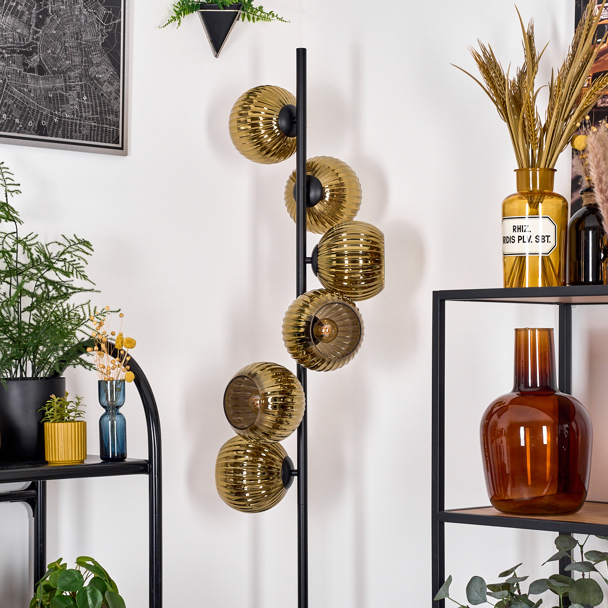 Ein modernes Zimmer mit einer Stehlampe mit goldenen Glaskugeln. Regale mit Pflanzen und Vasen befinden sich rechts und links.