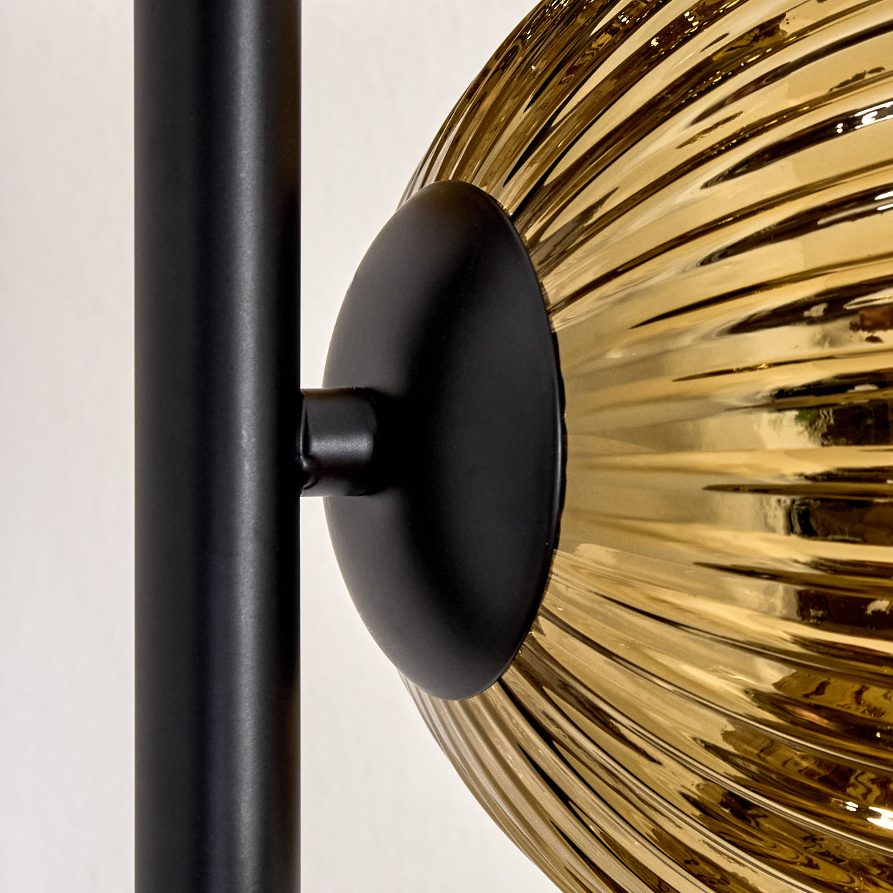 Nahaufnahme einer Lampe. Schwarzer Metallstiel und Halterung tragen einen strukturierten, bernsteinfarbenen Glasschirm. Der Hintergrund ist weiß.