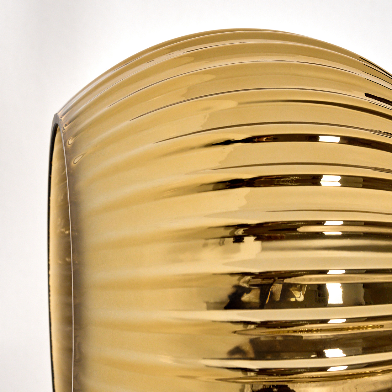 Nahaufnahme eines goldenen Glasobjekts. Es hat eine geriffelte Oberfläche und reflektiert Licht. Der Hintergrund ist weiß.