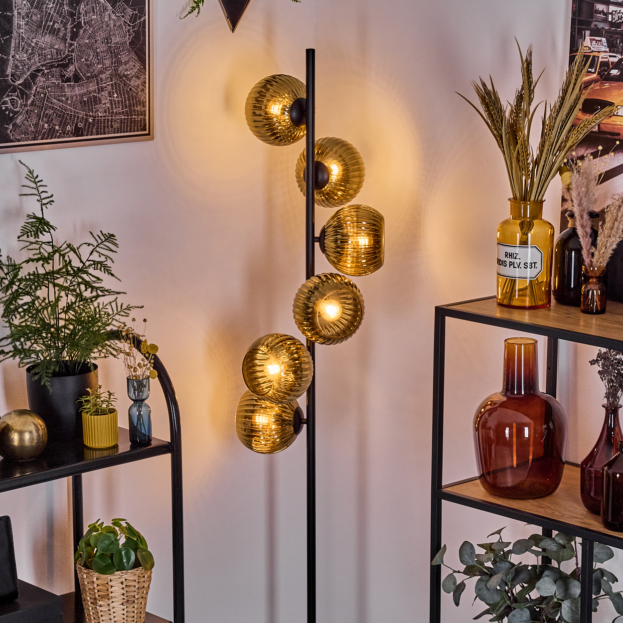 Ein modernes Wohnzimmer mit einer Stehlampe mit goldenen Kugeln, Regalen mit Pflanzen und Vasen und einem Kartenbild an der Wand.