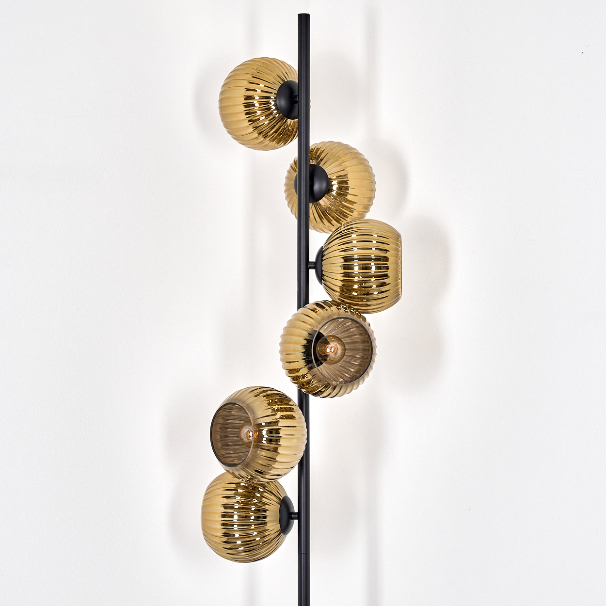 Eine moderne Wandlampe mit sechs goldenen Glaskugeln und einem schwarzen Metallrahmen vor einer weißen Wand.