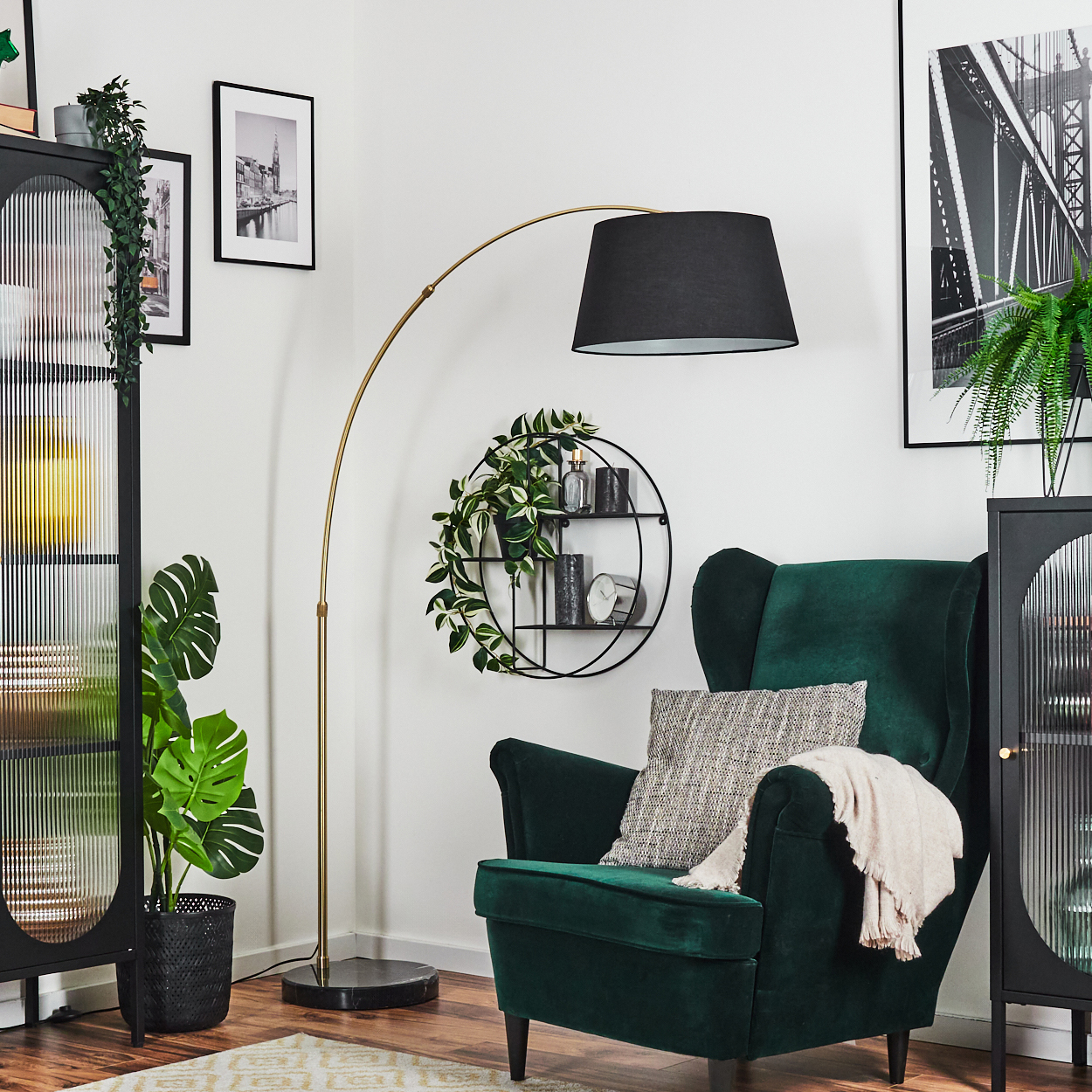Ein grüner Sessel mit Decke und Kissen steht neben einer Stehlampe und einem schwarzen Schrank mit Pflanzen und Bildern an der Wand.