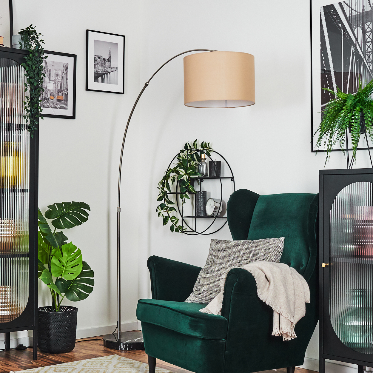 Ein grüner Sessel mit Decke und Kissen, eine Stehlampe und eine Pflanze in einem schwarzen Topf befinden sich in einem Raum.