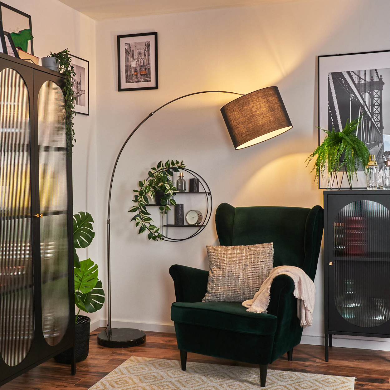 Ein dunkelgrüner Sessel mit Decke und Kissen, eine schwarze Lampe und ein schwarzer Schrank mit Pflanzen in einem Raum.