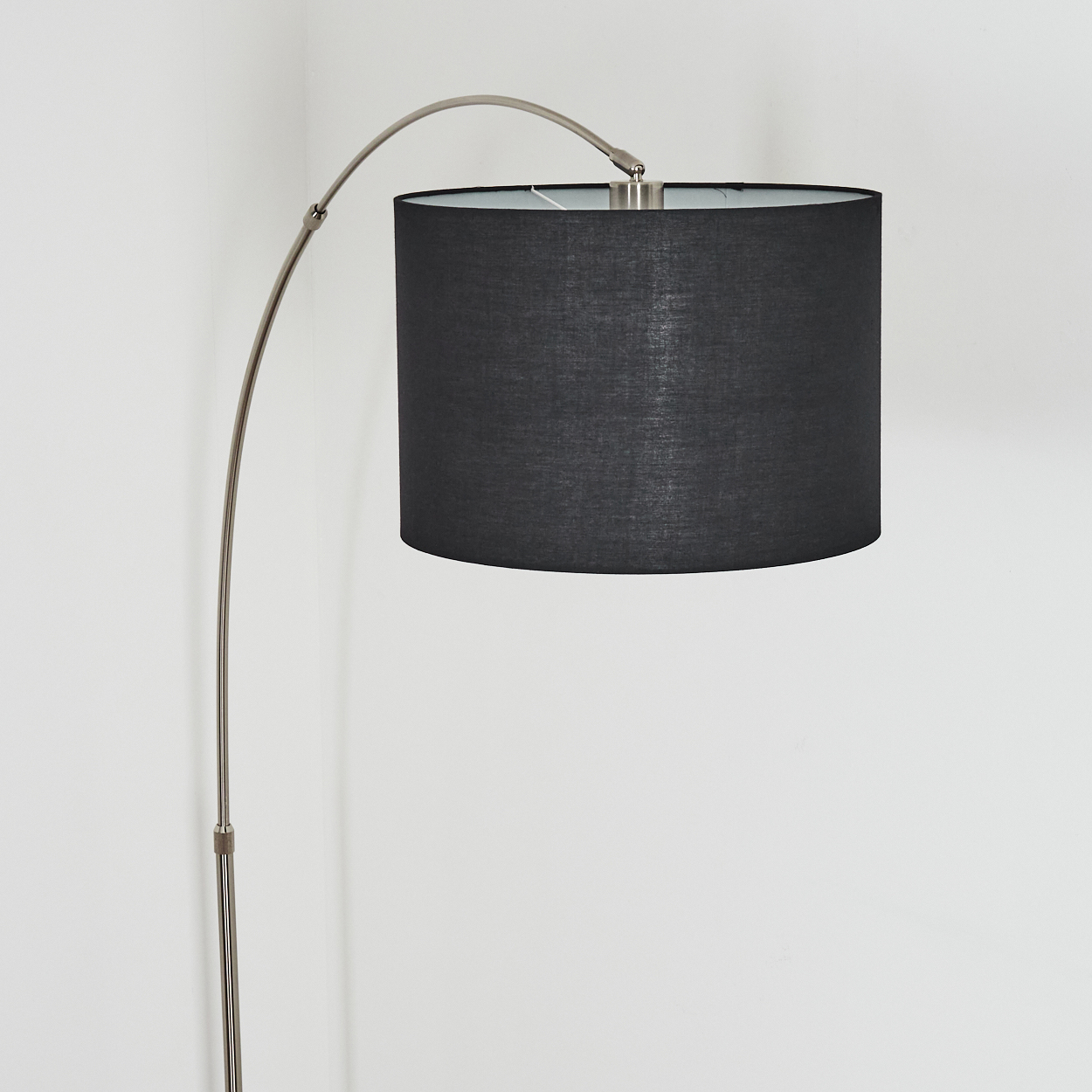 Eine moderne Bogen-Stehlampe mit schwarzem Schirm. Der Metallrahmen wölbt sich über, um den zylindrischen Schirm zu stützen.
