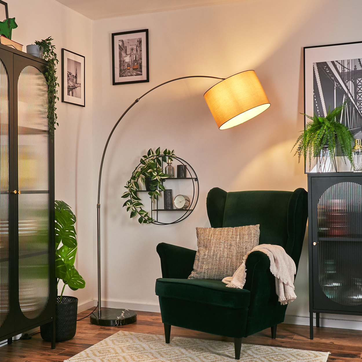 Ein grüner Sessel mit Kissen und Decke. Darüber eine Lampe. Pflanzen und Bilder sind im Hintergrund.