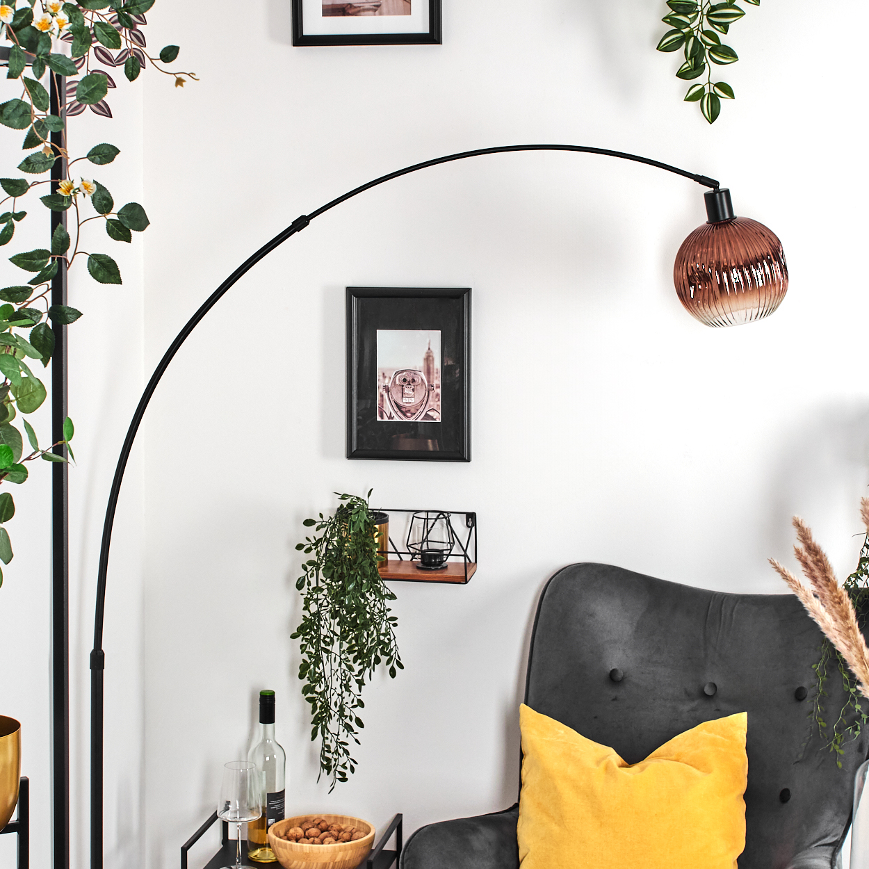 Ein modernes Wohnzimmer mit einer schwarzen Bogenlampe. Ein grauer Sessel hat ein gelbes Kissen. Ein kleiner Tisch hat eine Weinflasche und eine Schüssel mit Nüssen.