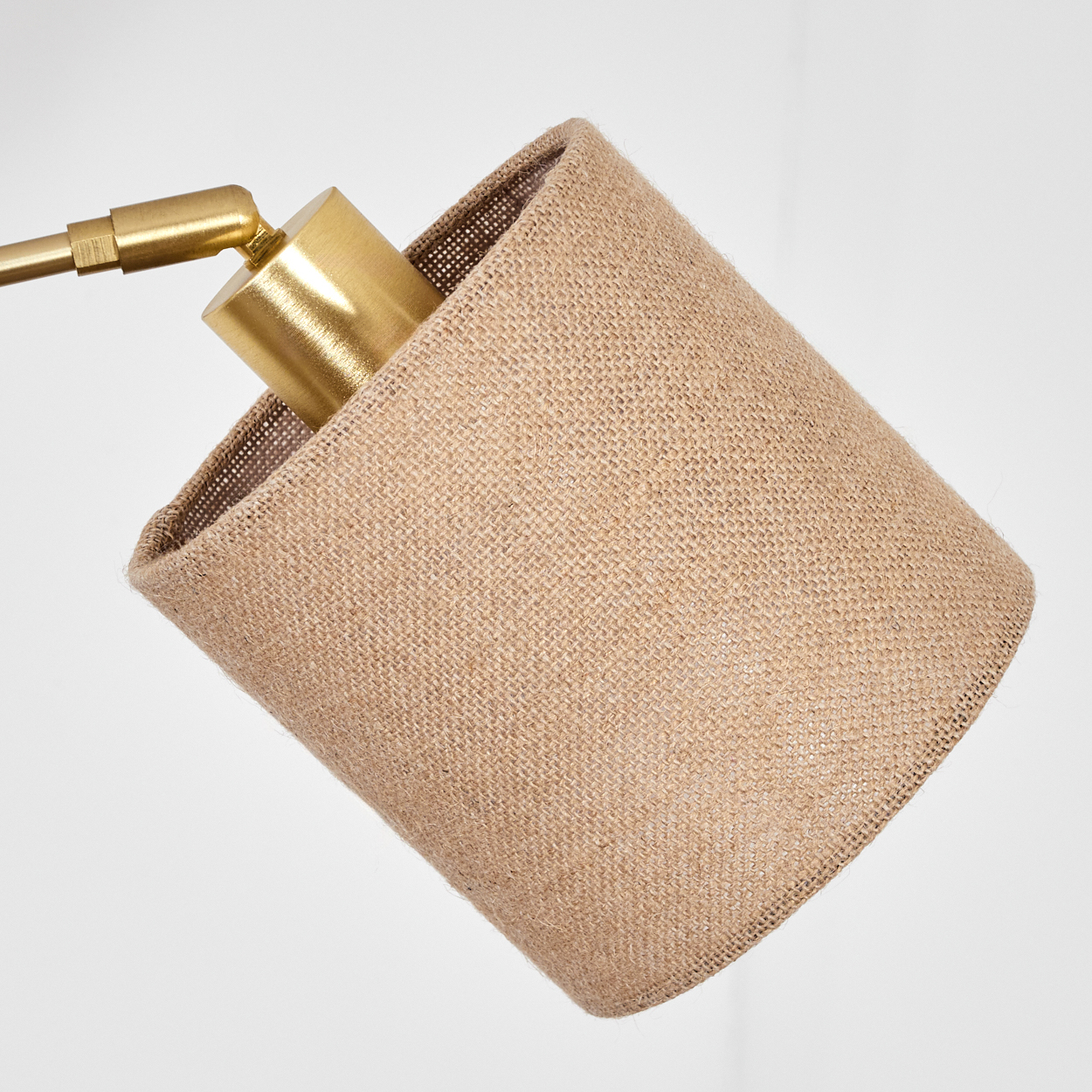 Nahaufnahme einer Lampe mit einem Lampenschirm aus Jute und Messingarmaturen vor weißem Hintergrund.