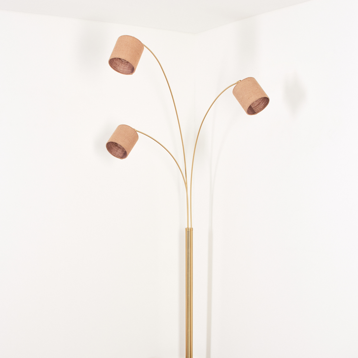Eine Stehlampe mit drei Lampenschirmen. Die Lampe hat einen goldenen Fuß und gebogene Arme. Die Lampenschirme sind zylindrisch und beige.