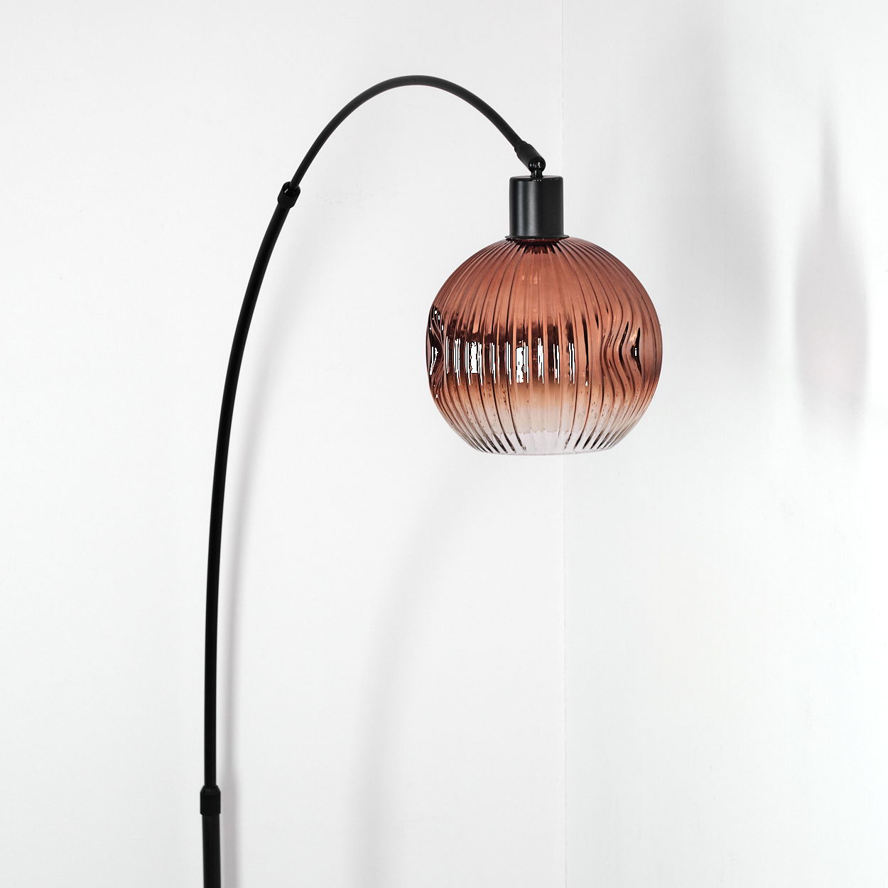 Eine moderne Stehlampe mit schwarzem, gebogenem Arm und geripptem, bernsteinfarbenem Glasschirm. Der Hintergrund ist eine weiße Wand.