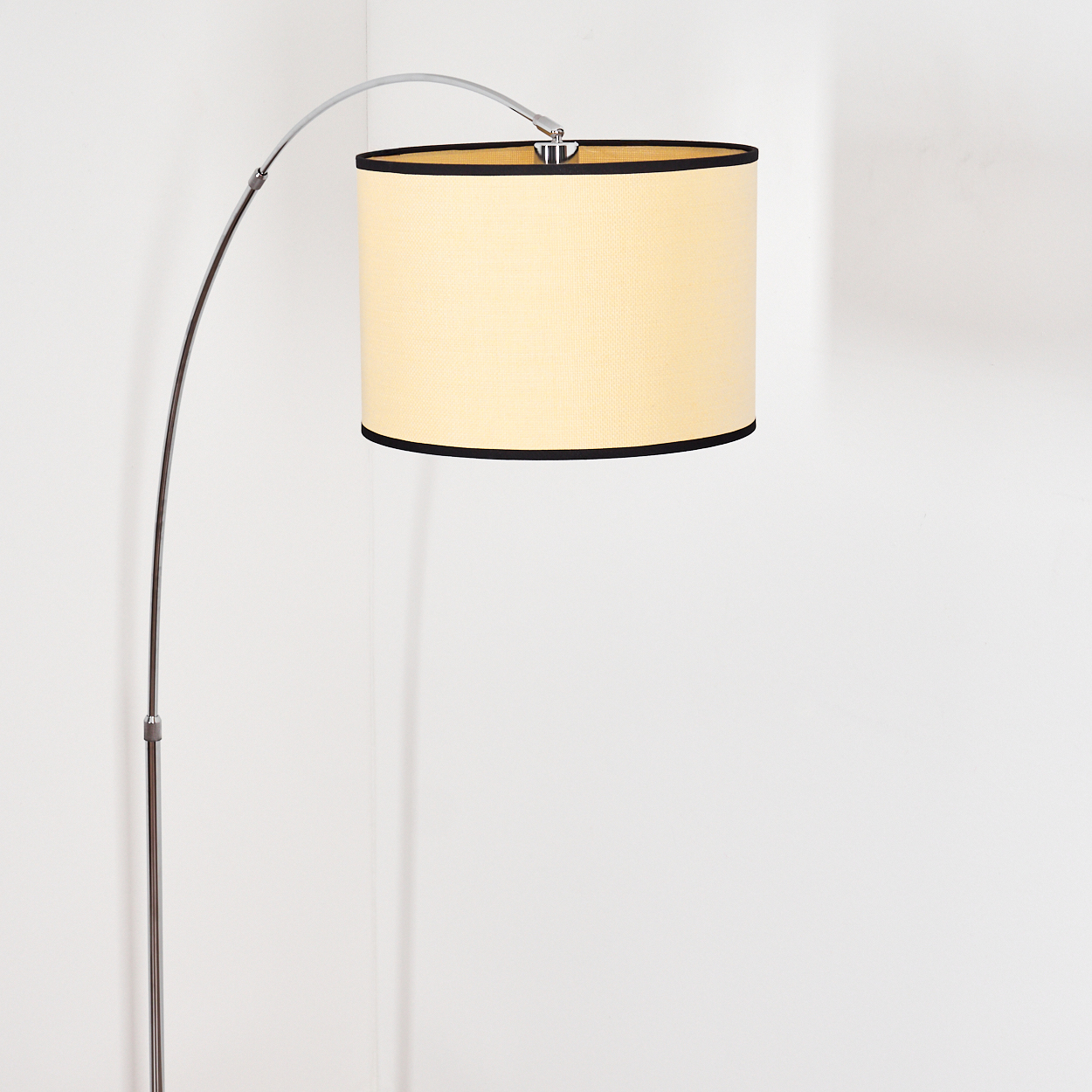 Eine moderne Bogenlampe mit cremefarbenem Lampenschirm und schwarzer Einfassung. Die Lampe steht vor weißem Hintergrund.
