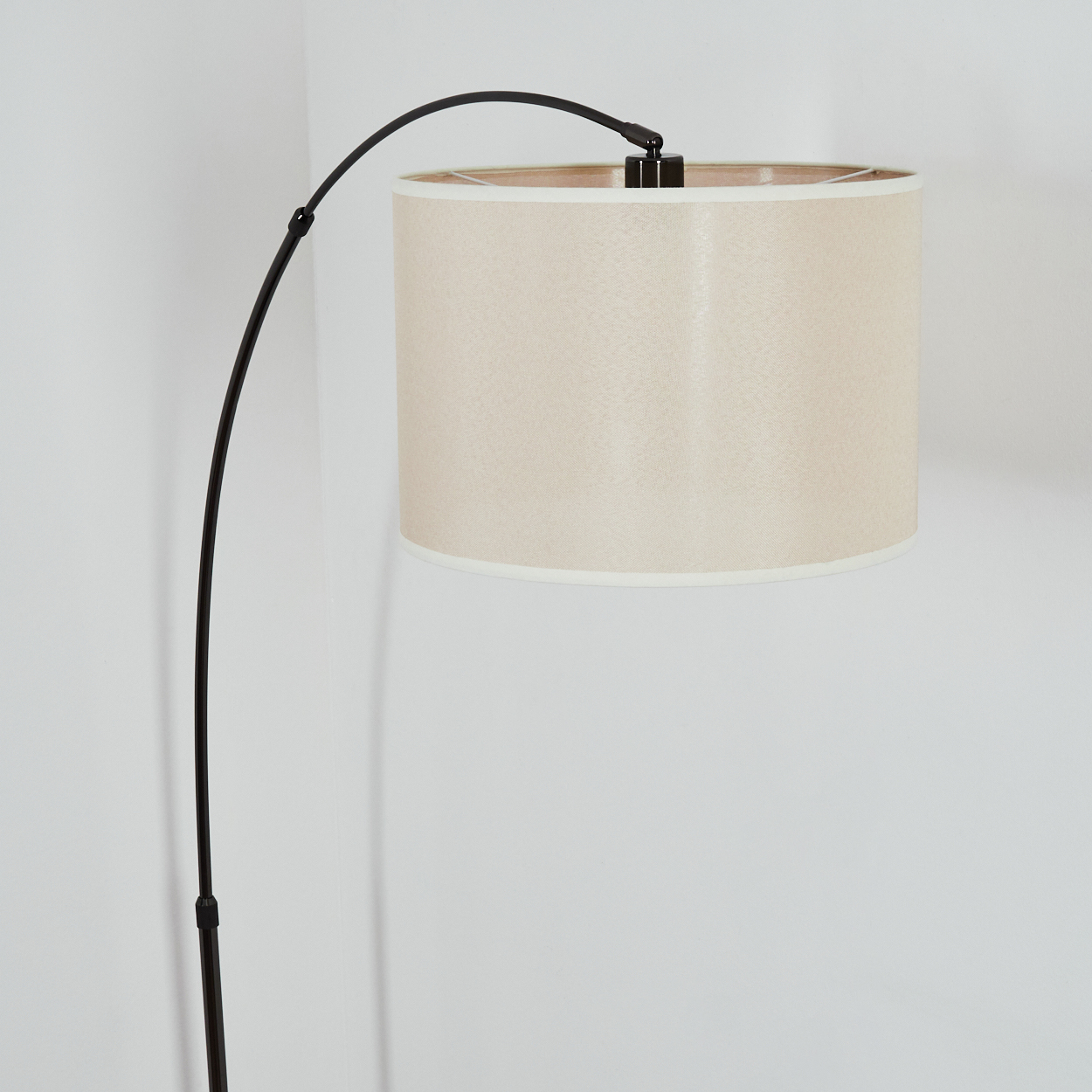 Eine moderne Stehlampe mit schwarzem gebogenen Arm und beigem Lampenschirm steht vor einer weißen Wand.