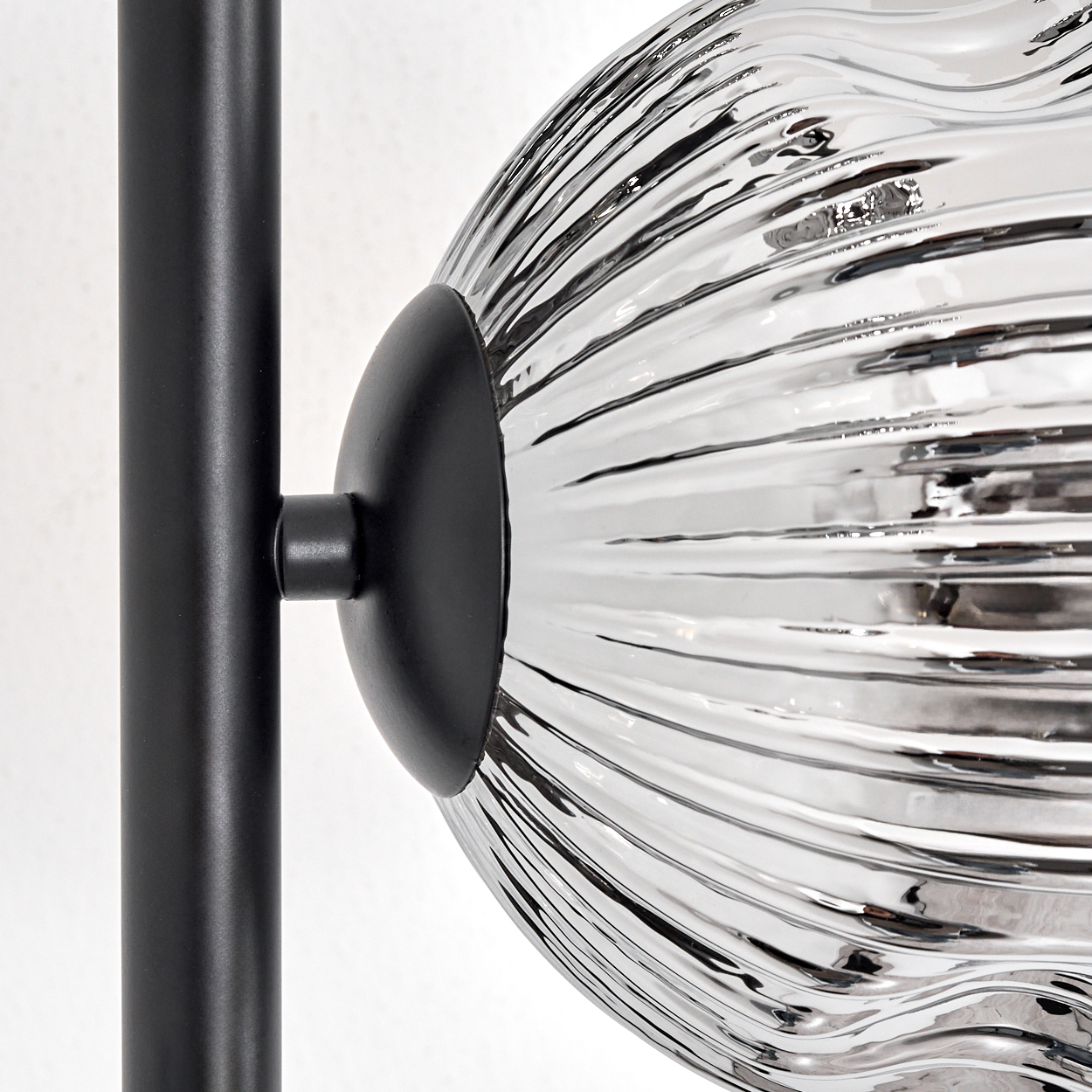 Nahaufnahme einer Lampe. Ein schwarzer Metallstab trägt einen kugelförmigen, gerippten Glasschirm. Der Schirm ist mit einer schwarzen Armatur am Stab befestigt.