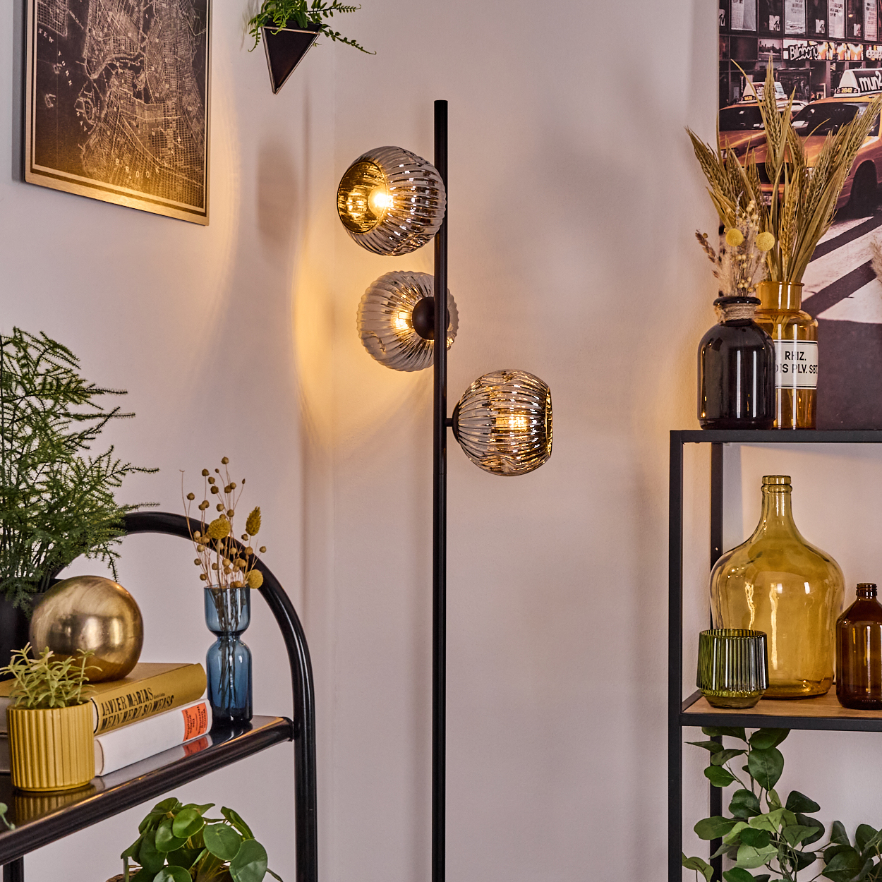 Ein modernes Zimmer mit einer schwarzen Lampe mit drei Glaskugeln, Regalen mit Dekorationen, einer Karte und einer Pflanze.