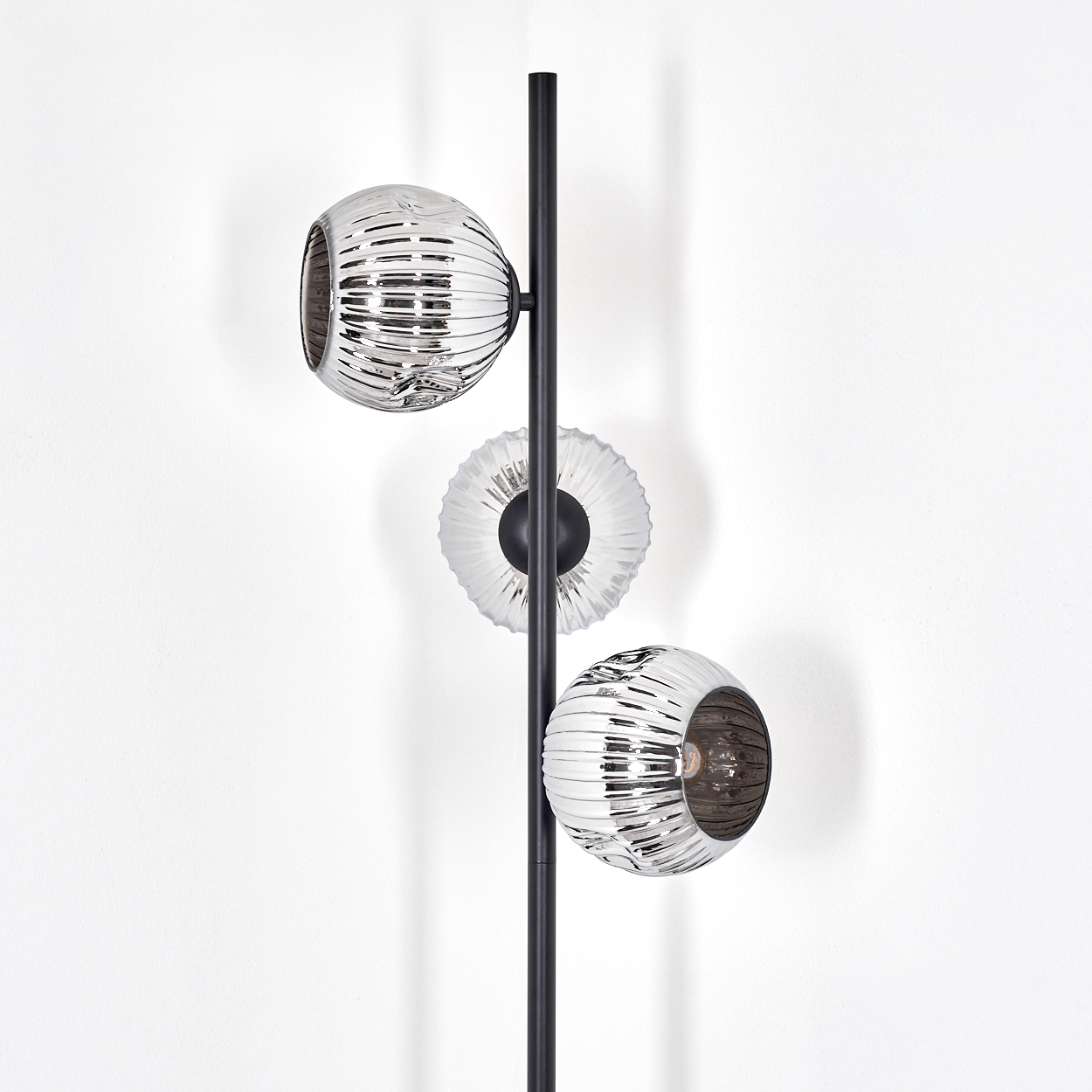 Eine moderne Lampe mit schwarzem Pfosten und drei Glasschirmen. Die Schirme sind reflektierend, der Hintergrund ist weiß.