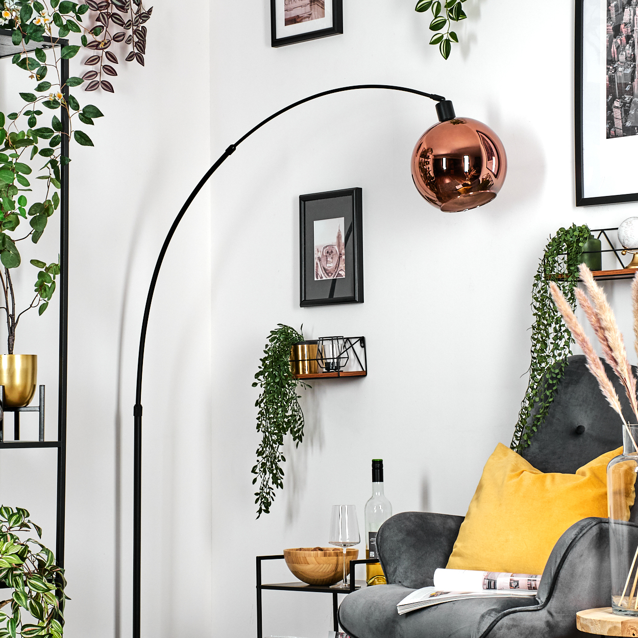Ein modernes Wohnzimmer mit einer Kupferlampe, einem grauen Sessel mit gelbem Kissen und dekorativen Pflanzen.