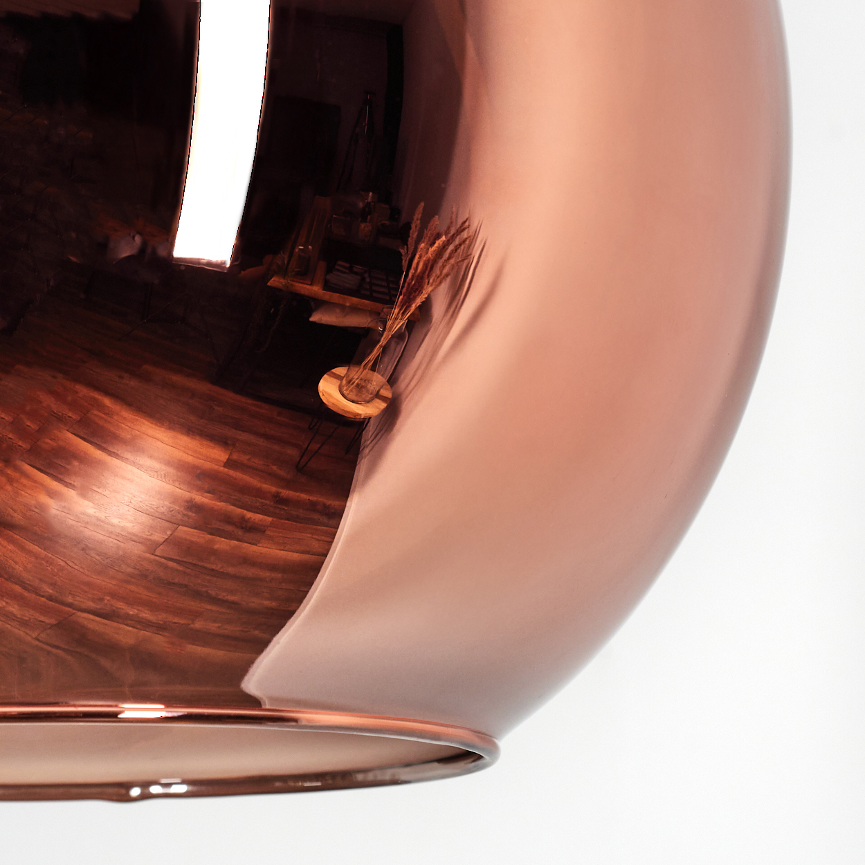Eine kupferfarbene, reflektierende Oberfläche. Die Reflexion zeigt einen Raum mit Holzböden und einem Tisch mit einer Weizenvase.