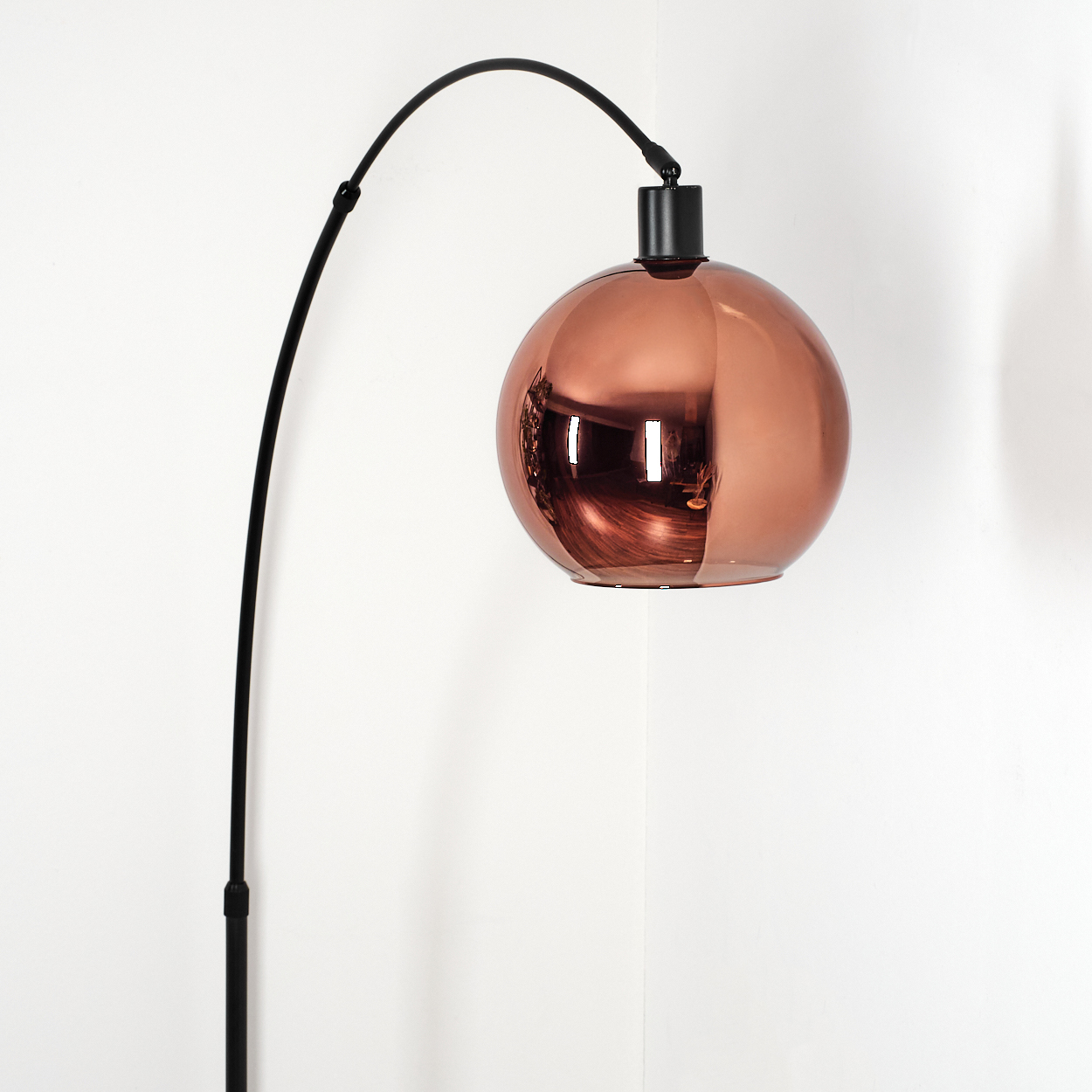 Eine moderne Stehlampe mit schwarzem, gebogenem Stiel und großem, kupferfarbenem, kugelförmigem Lampenschirm. Der Hintergrund ist eine weiße Wand.