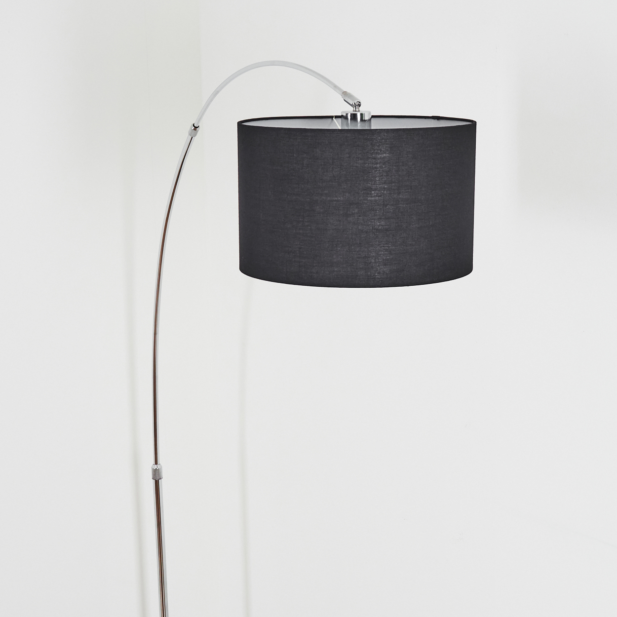 Eine moderne Bogen-Stehlampe mit schwarzem Lampenschirm. Die Lampe hat einen silberfarbenen Metallrahmen und steht vor einer weißen Wand.