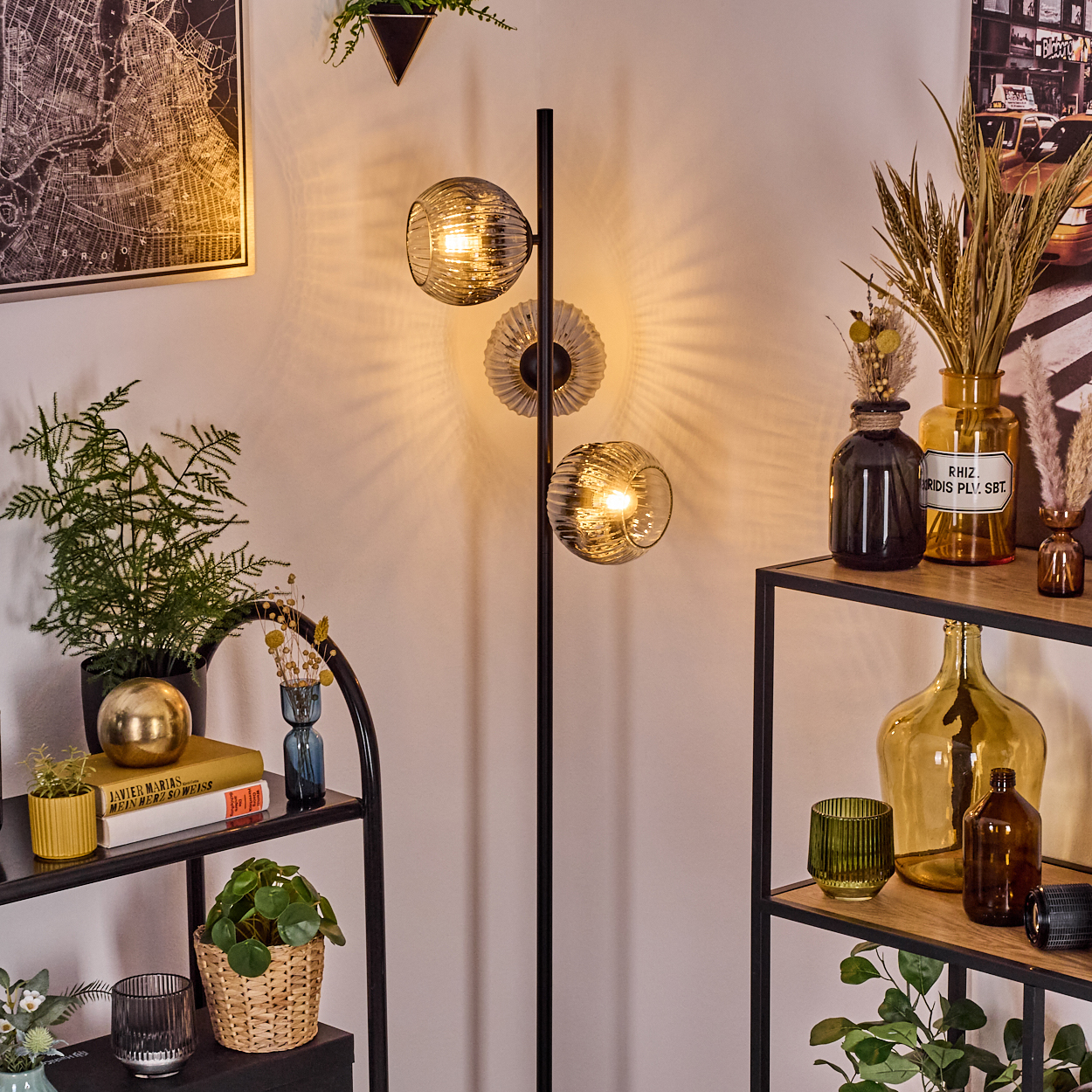 Ein modernes Wohnzimmer mit Stehlampe. Regale zeigen Pflanzen und Dekor. Eine Karte und ein Bild an der Wand.