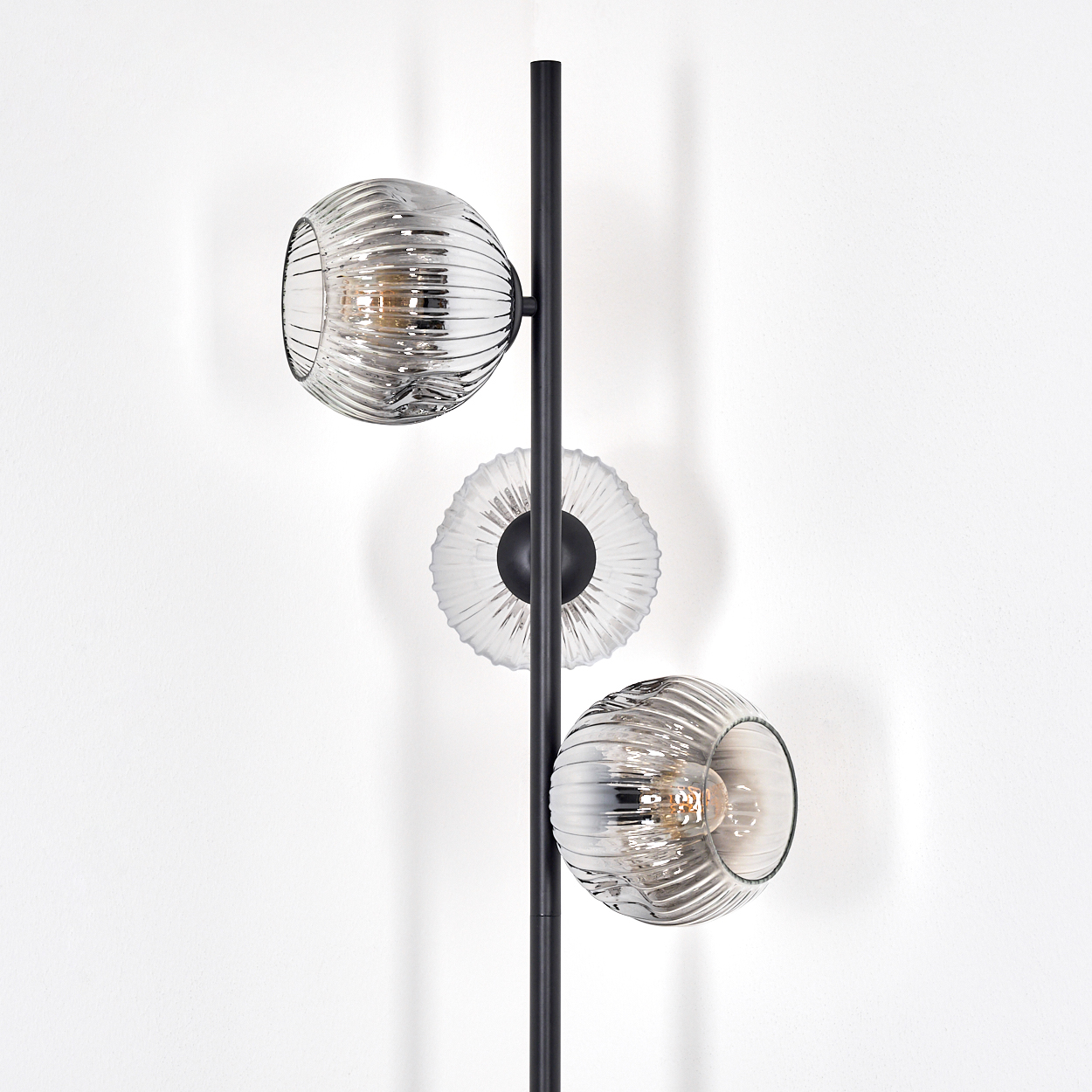 Eine moderne Lampe mit drei Glaskugeln. Die Lampe ist schwarz und der Hintergrund ist eine weiße Wand.