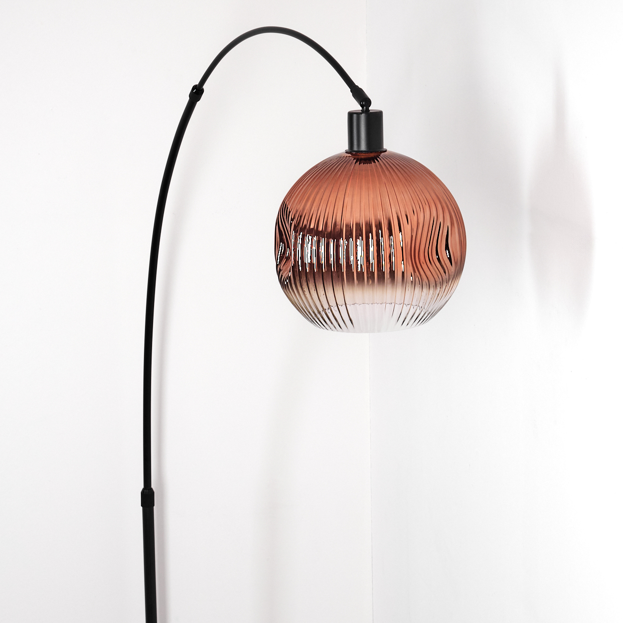 Eine moderne Stehlampe mit schwarzem, gebogenem Rahmen und braunem, geripptem Glasschirm vor weißer Wand.