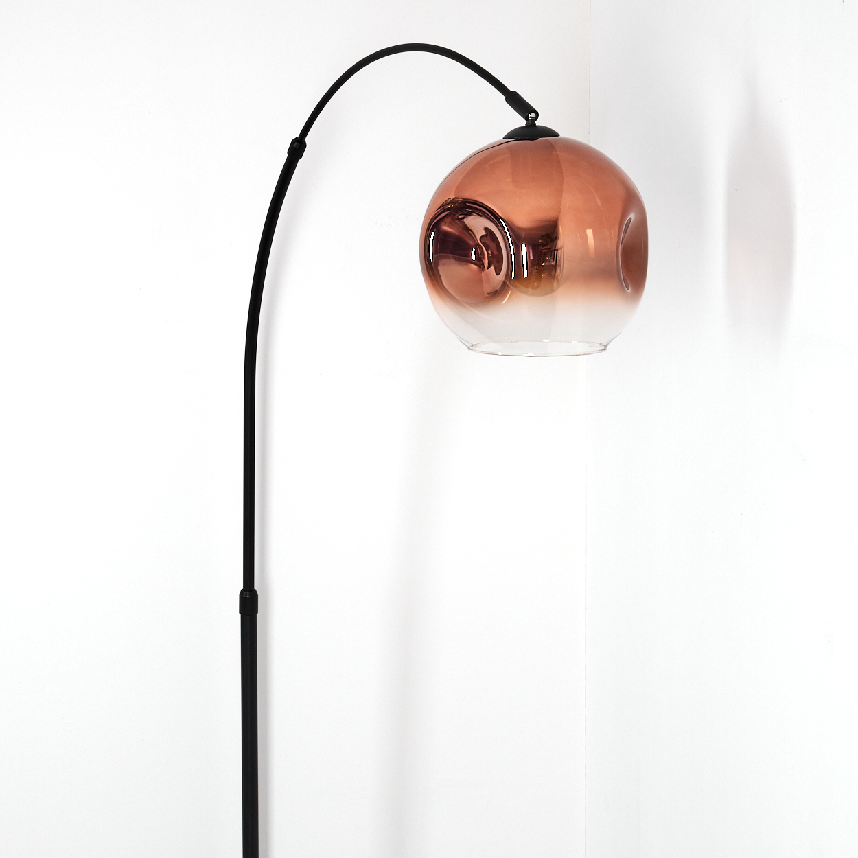 Eine moderne Stehlampe mit einem schwarzen, gebogenen Arm und einem kugelförmigen, farbverlaufenden Lampenschirm. Der Hintergrund ist eine weiße Wand.