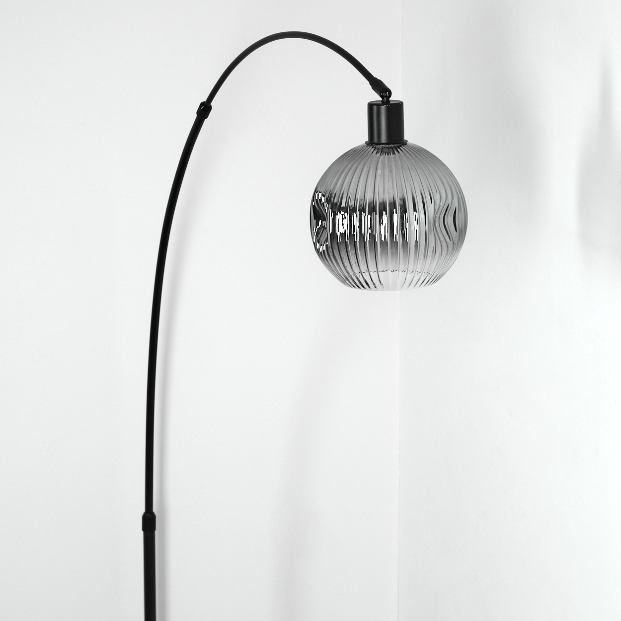 Eine moderne schwarze Stehlampe mit gebogenem Arm und Glasschirm vor weißer Wand.