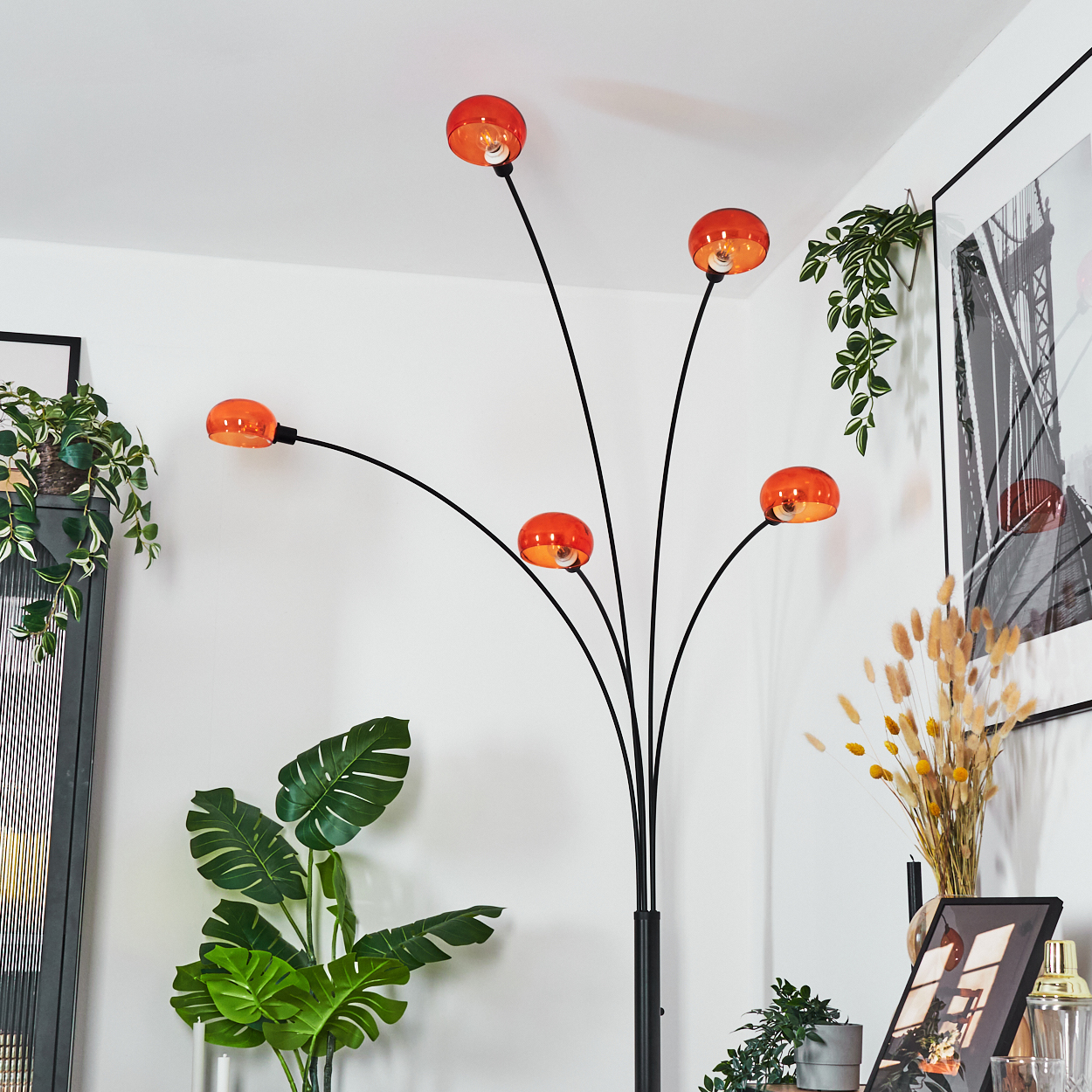 Eine moderne Stehlampe mit fünf orangefarbenen Kugeln. Pflanzen und gerahmte Kunstwerke umgeben sie, vor einer weißen Wand.