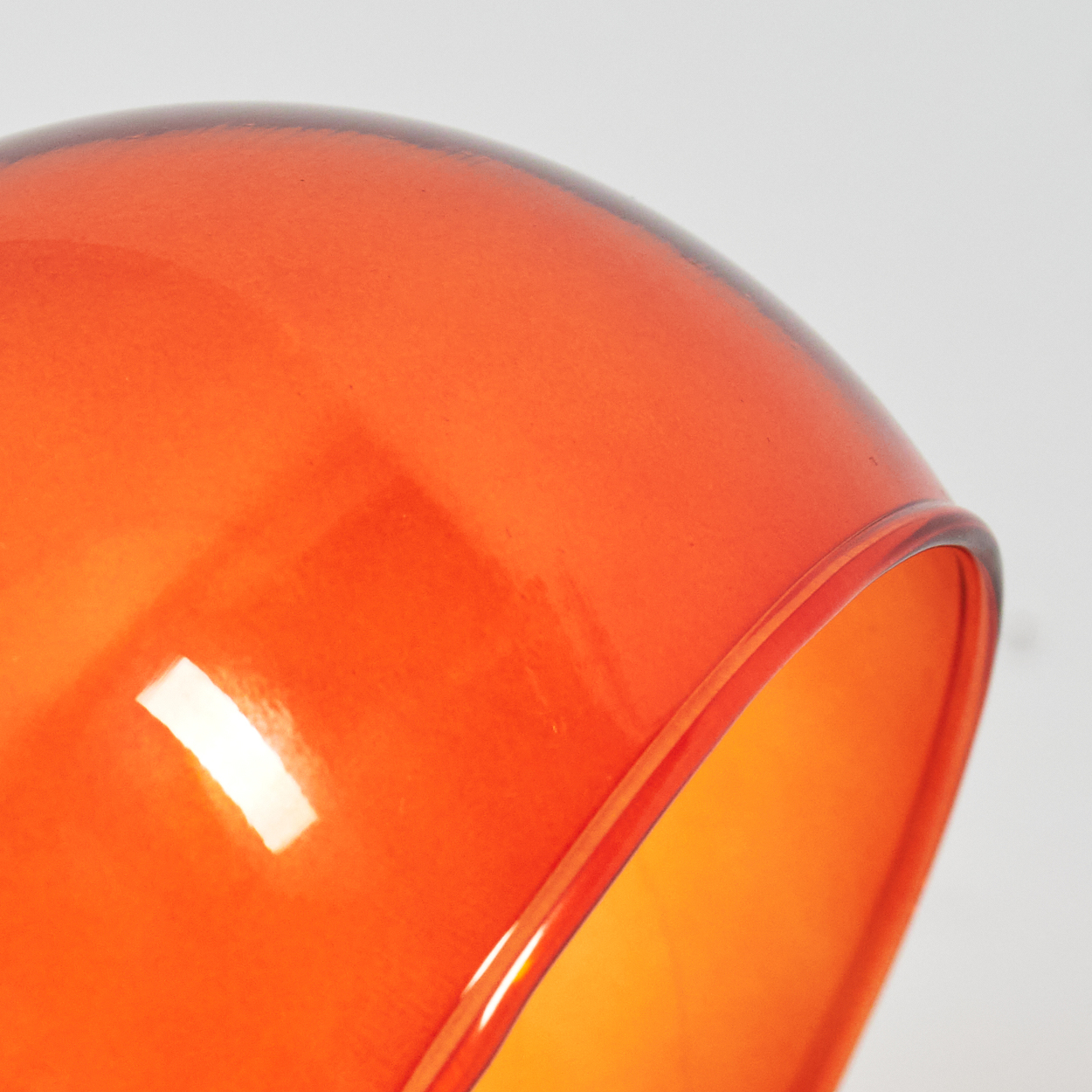 Nahaufnahme eines leuchtend orangefarbenen Glasschirms vor weißem Hintergrund. Das Innere leuchtet heller orange.