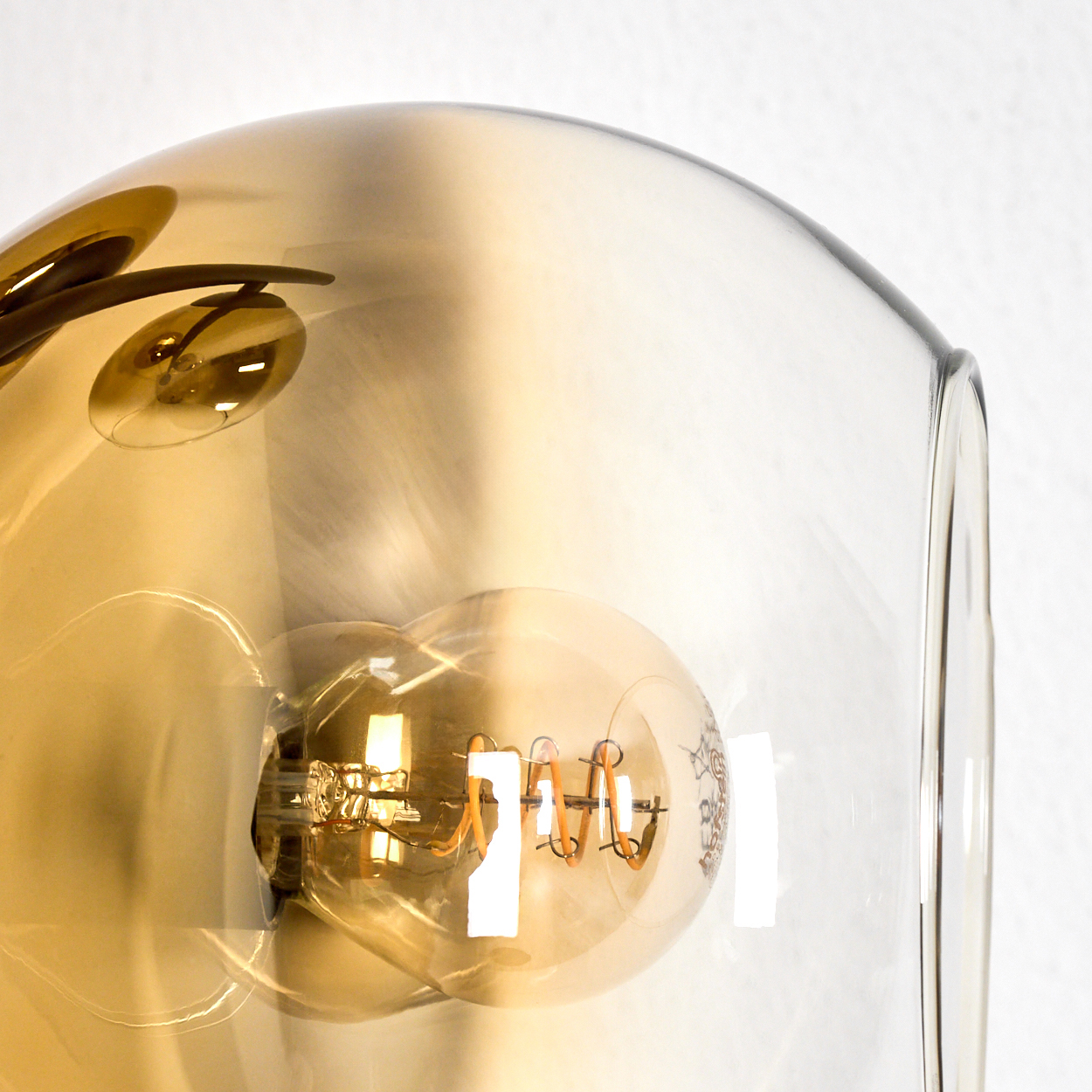 Nahaufnahme einer Leuchte mit einer Glühbirne in einem Glasschirm. Die Glühbirne hat einen Spiralglühfaden. Der Schirm ist bernsteinfarben.