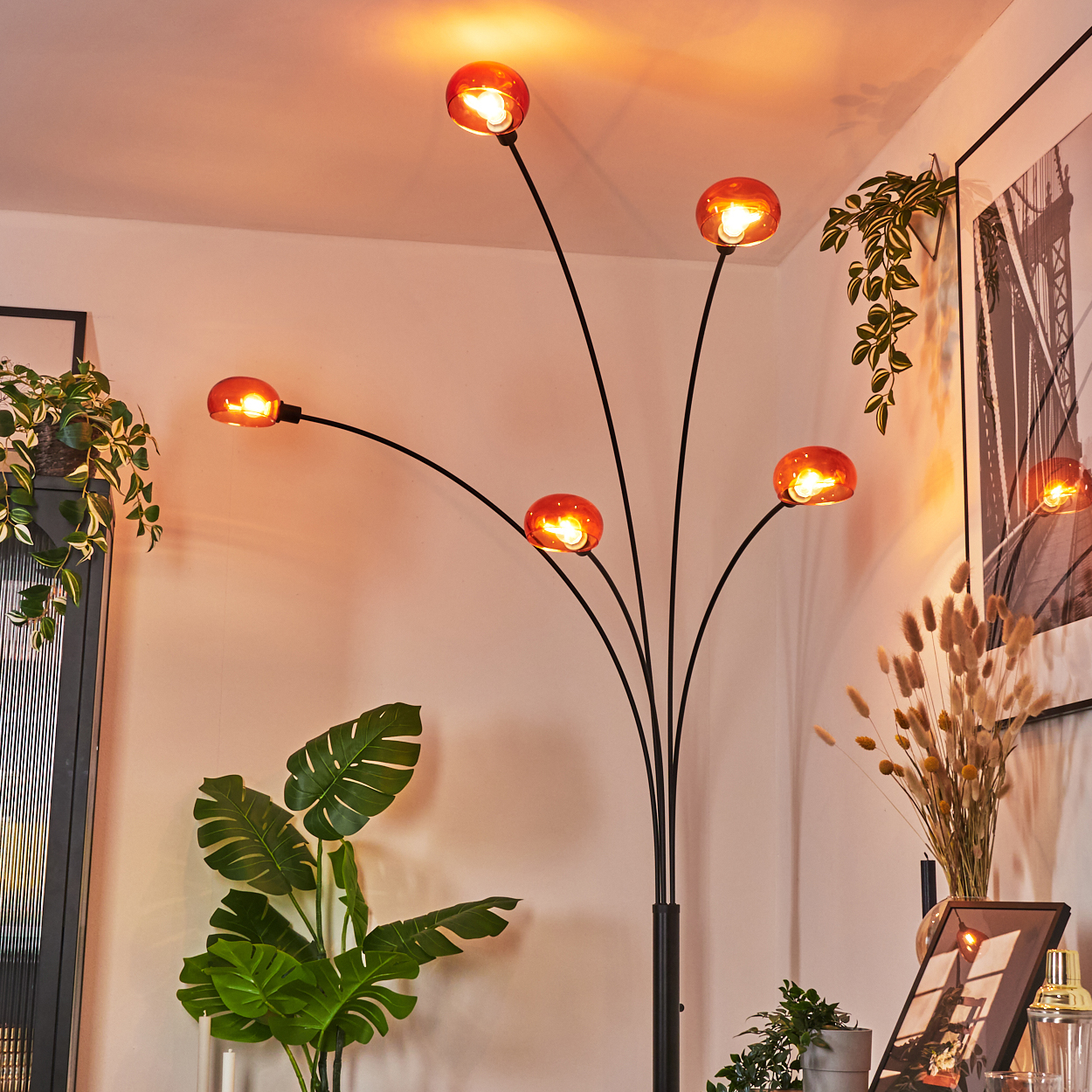 Eine moderne Stehlampe mit fünf orangefarbenen Glasschirmen. Pflanzen und Kunstwerke im Hintergrund schaffen eine warme Atmosphäre.